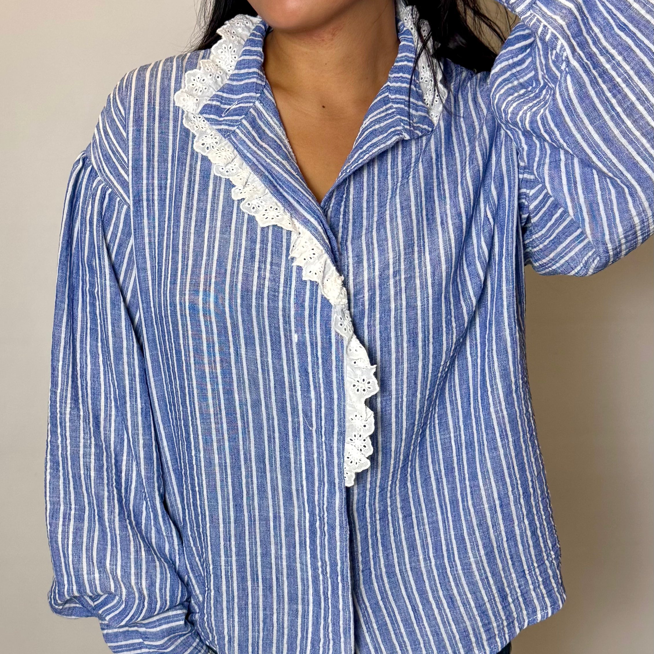 Woman wearing a blue and white striped shirt with lace trim against a beige background