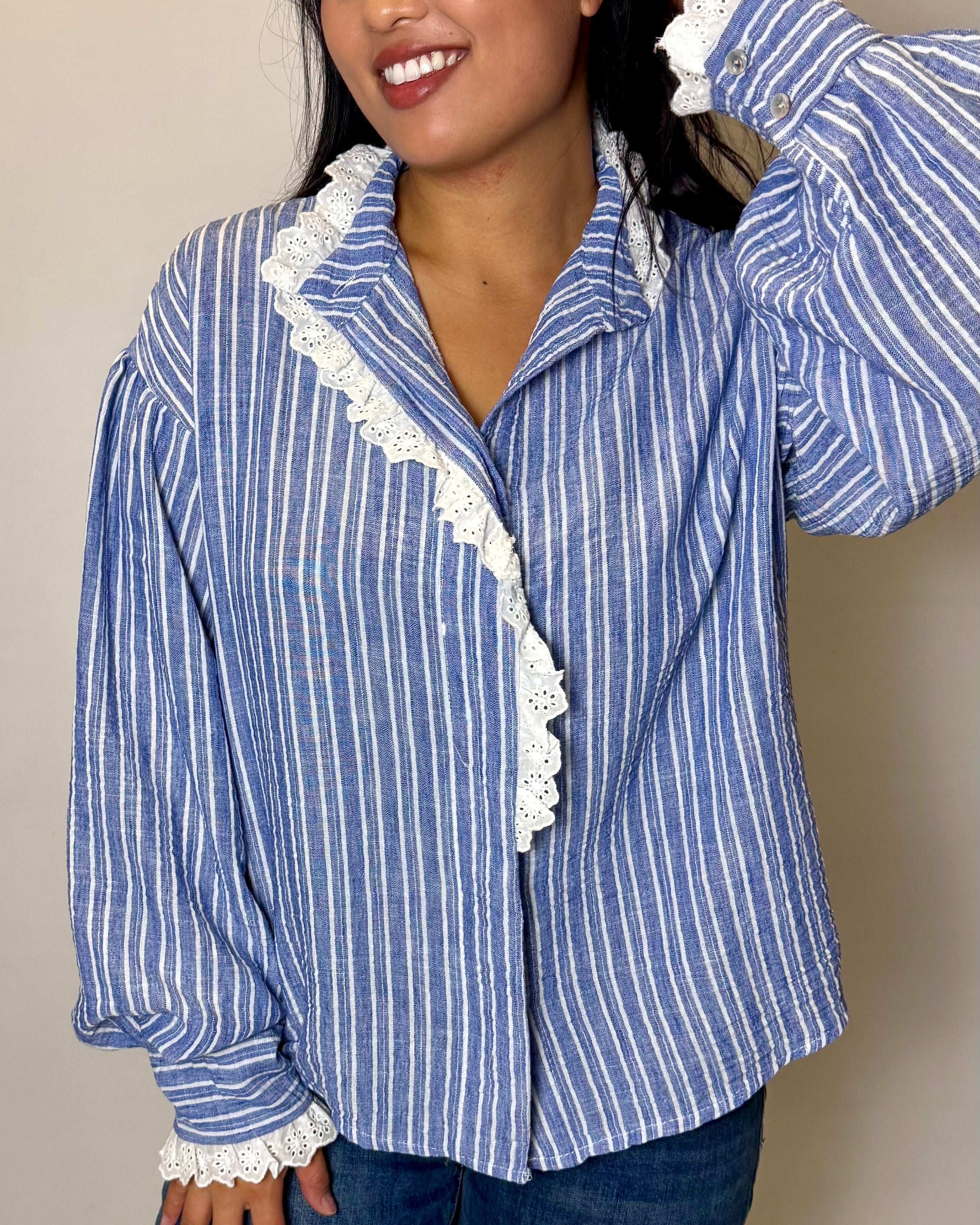 Woman wearing a blue and white striped shirt with lace trim against a beige background