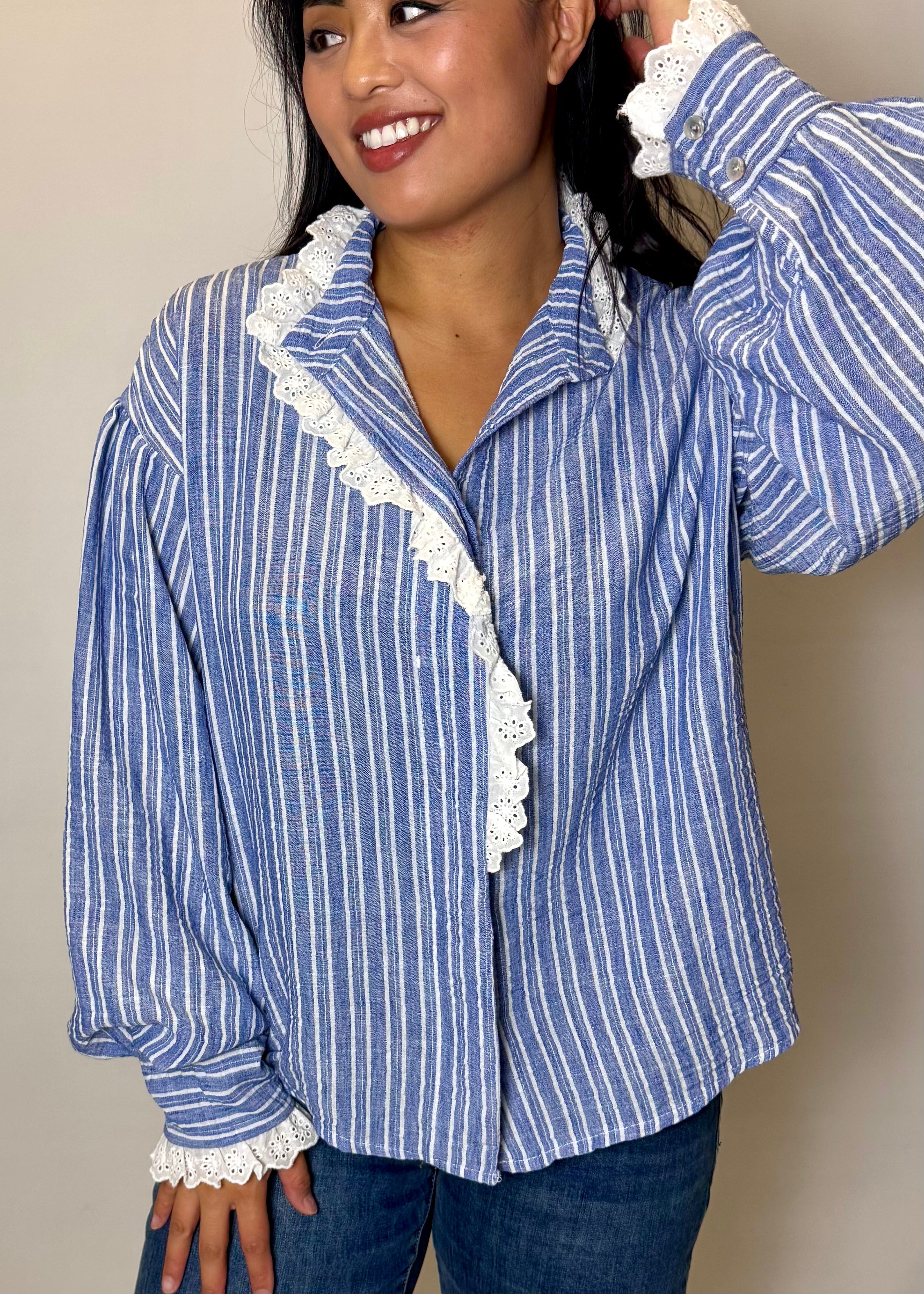 Woman wearing a blue and white striped shirt with lace trim against a beige background