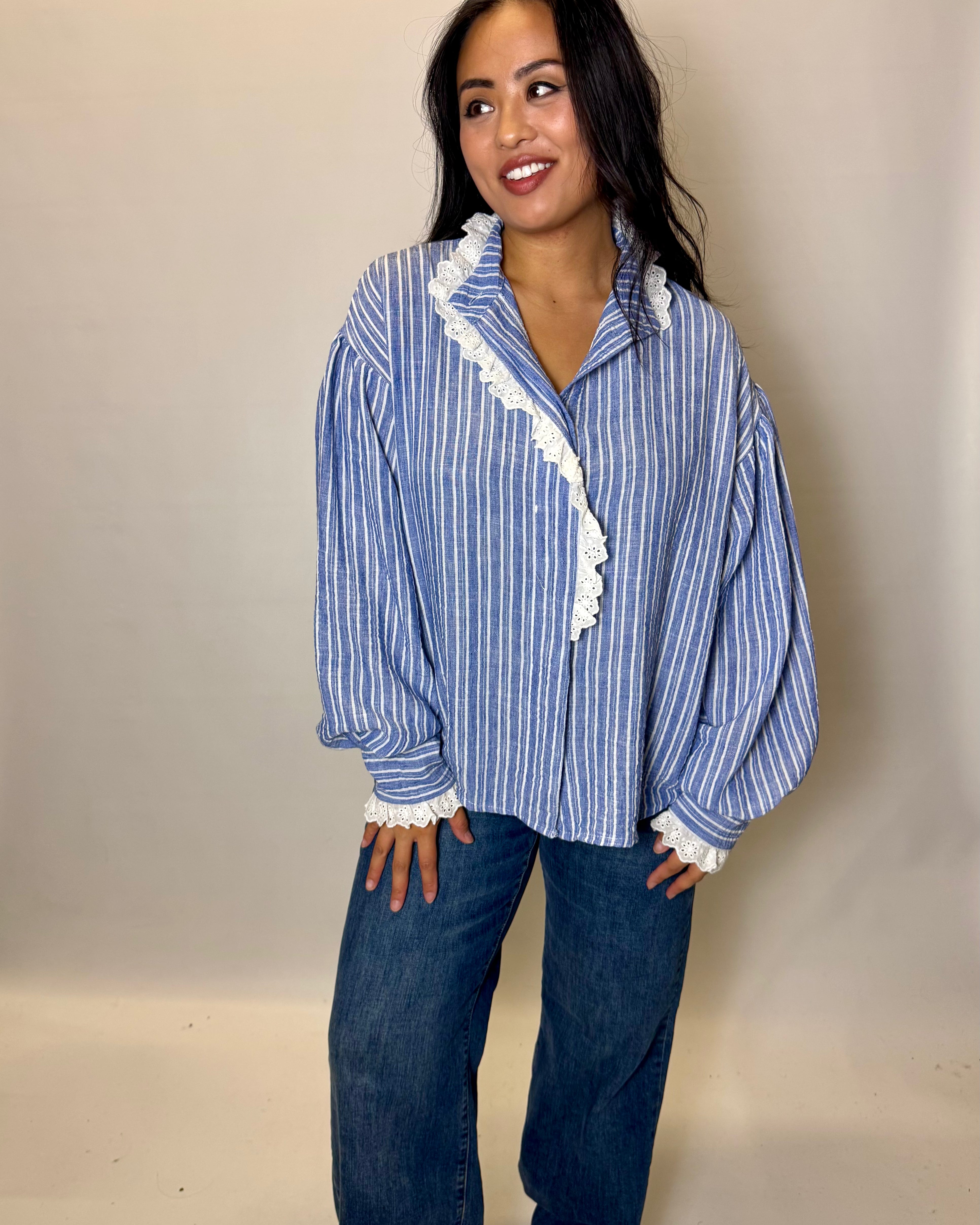 Woman wearing a blue and white striped shirt with lace trim and jeans against a beige background