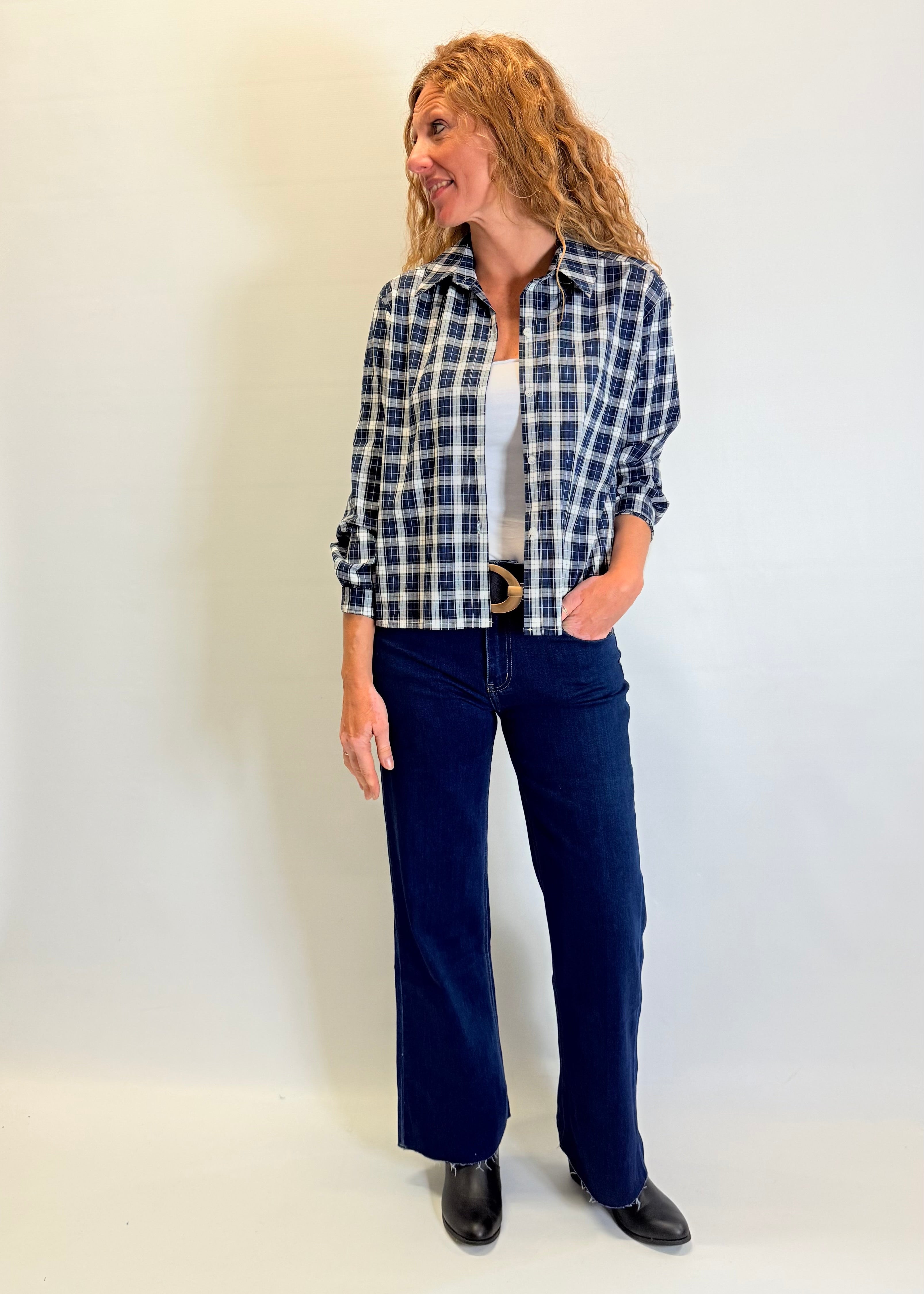 Woman wearing a plaid shirt and blue jeans against a white background