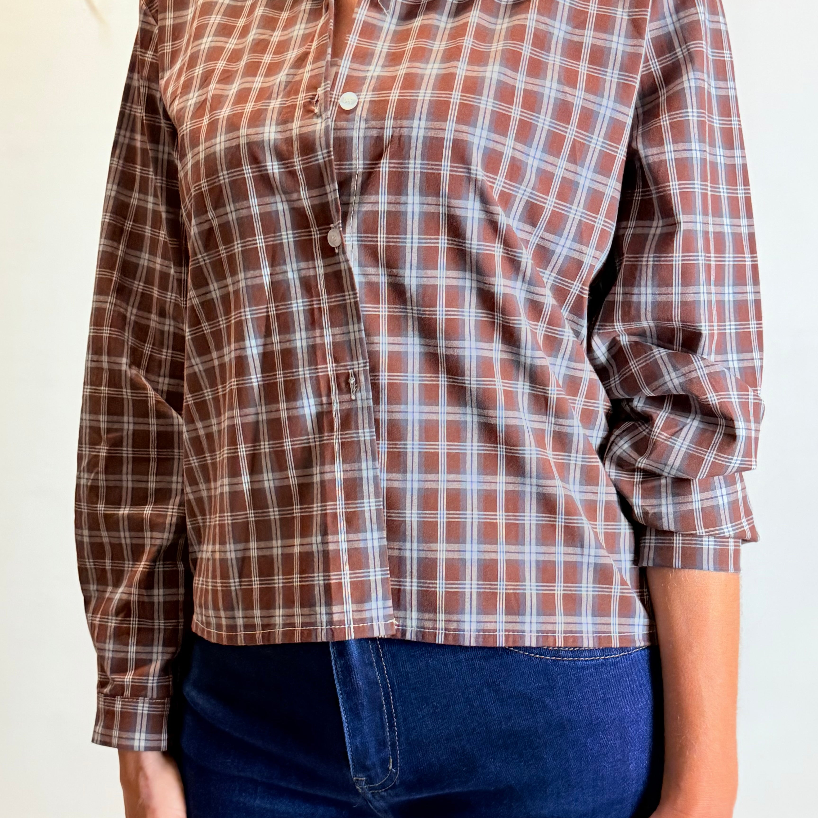 Person wearing a brown plaid shirt and blue jeans on a plain background