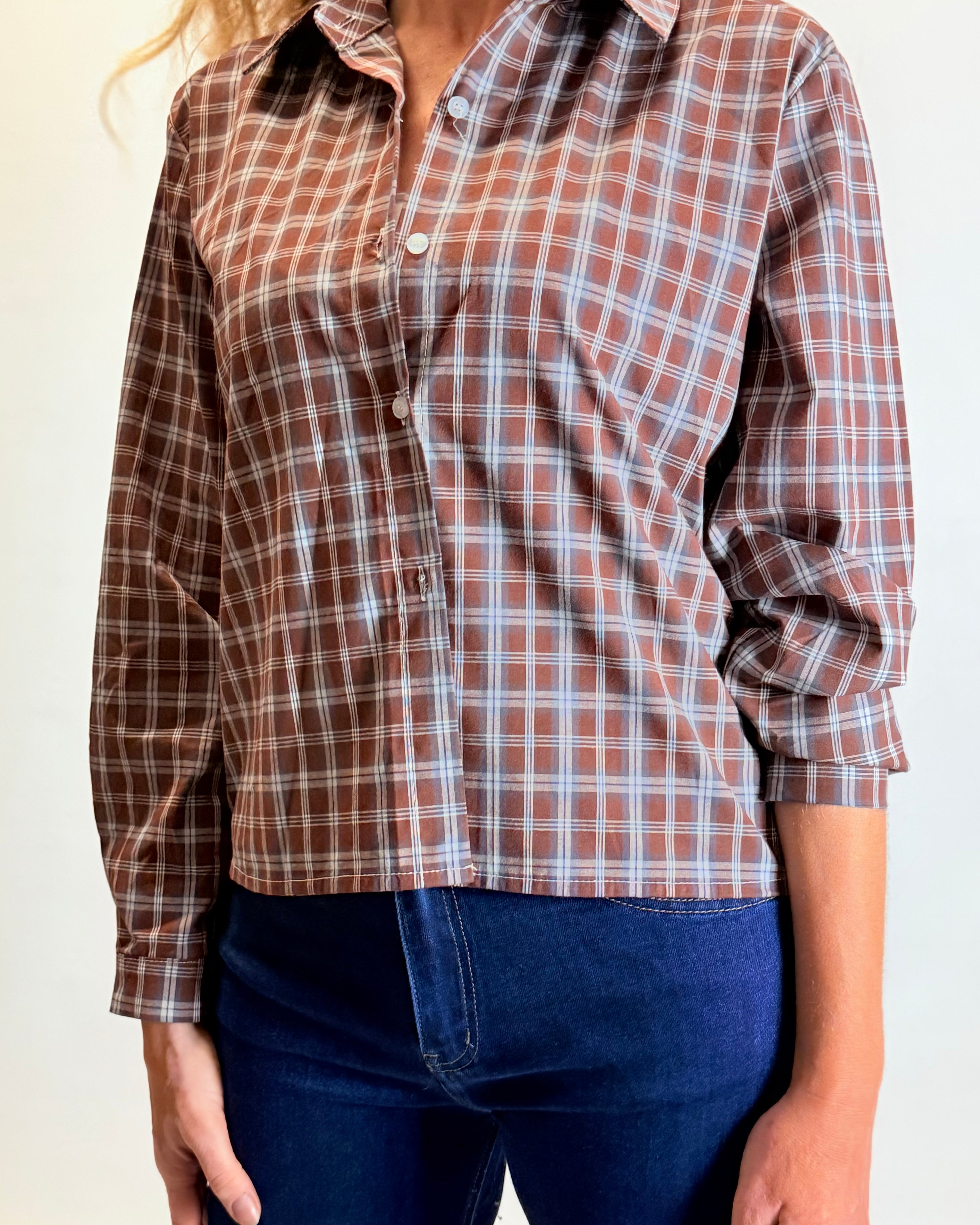 Person wearing a brown plaid shirt and blue jeans on a plain background