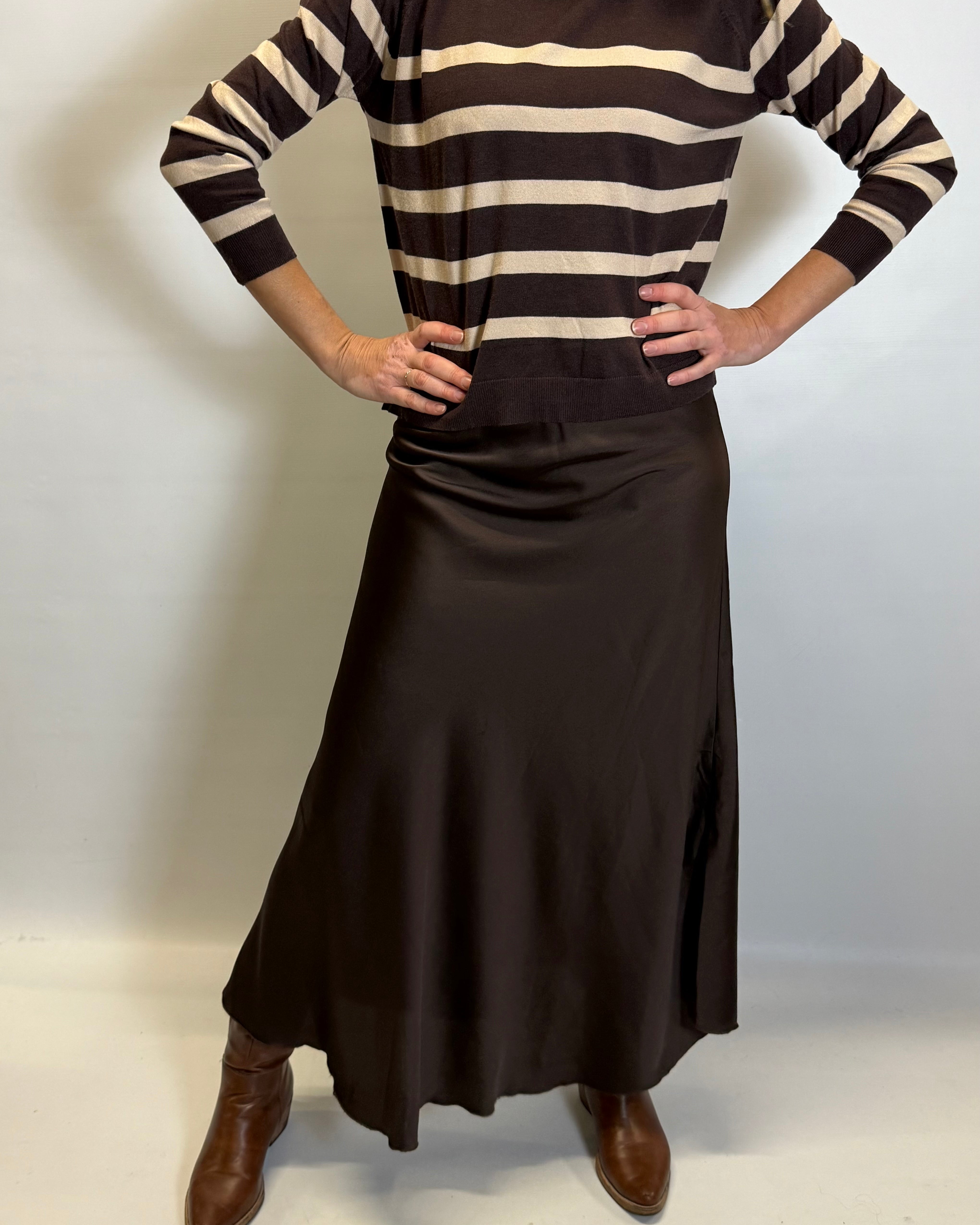 Person wearing a brown and beige striped sweater with a long brown skirt on a white background