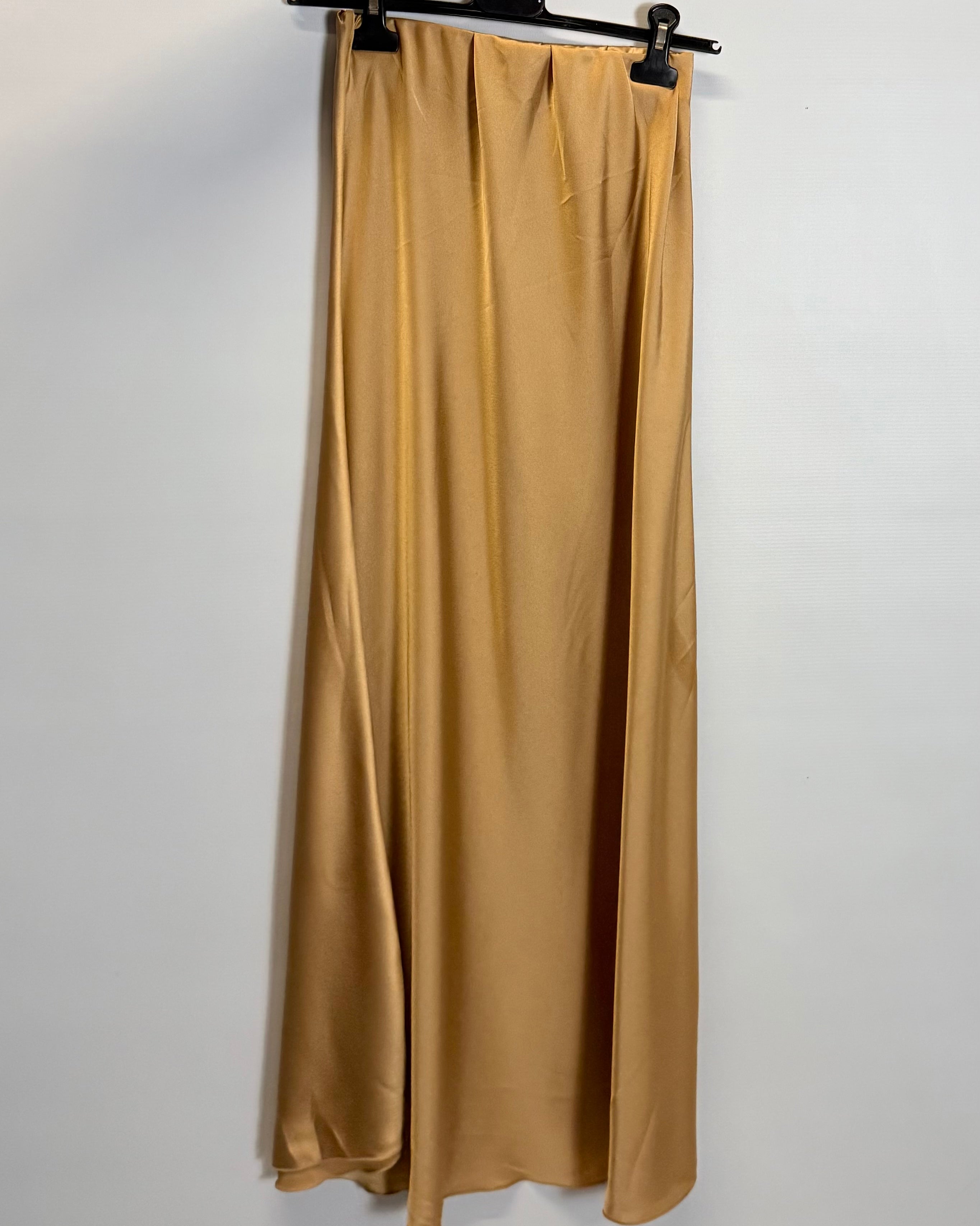 Gold satin skirt hanging on a hanger against a white background