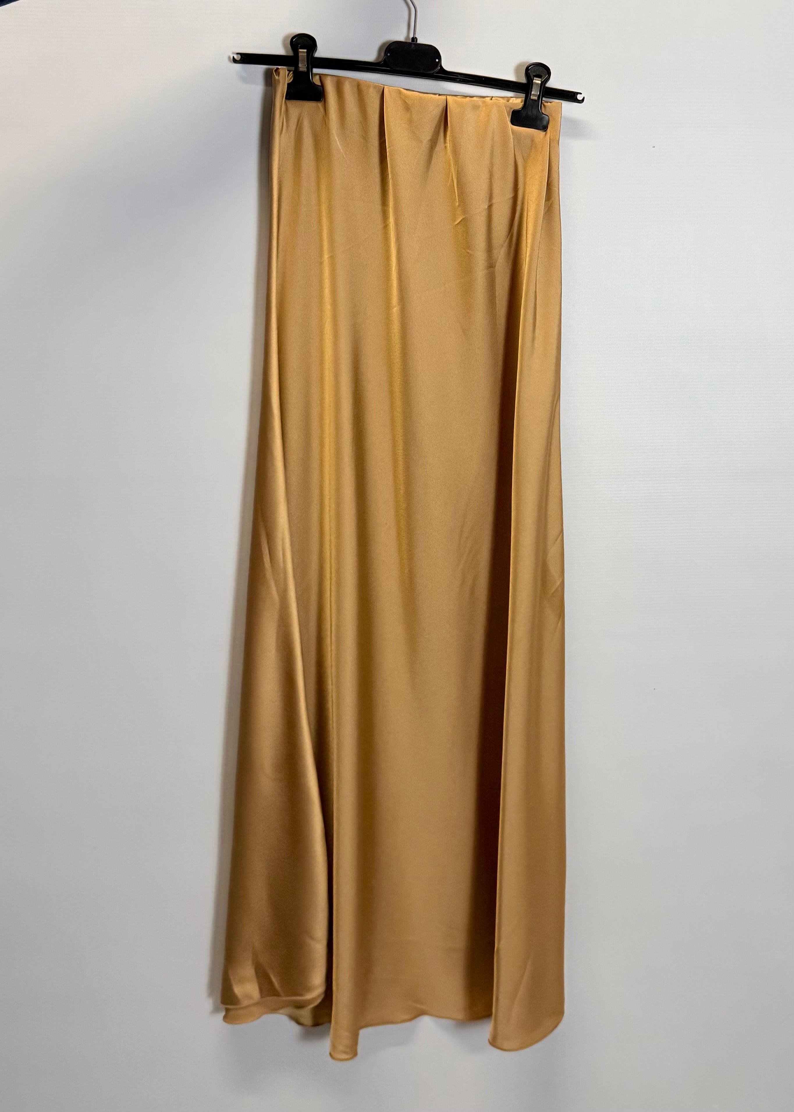 Gold satin skirt hanging on a hanger against a white background