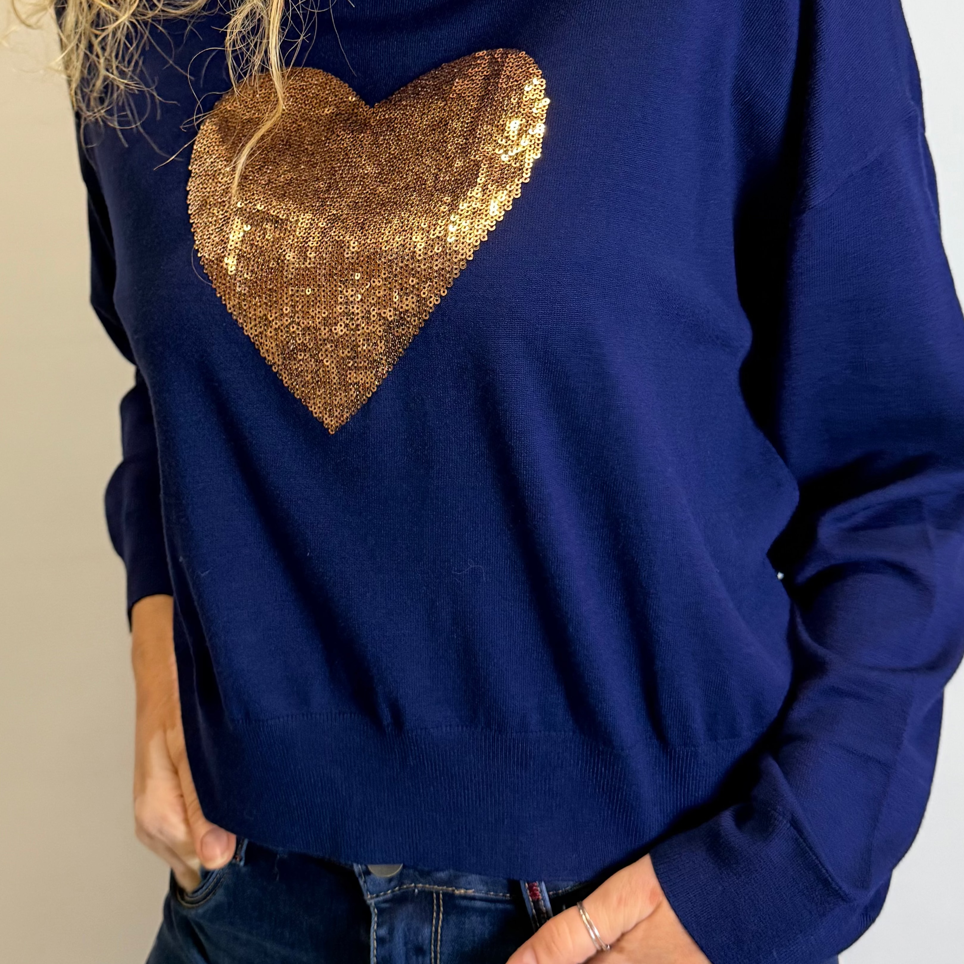 Woman wearing a blue sweater with a gold sequin heart design on a plain background