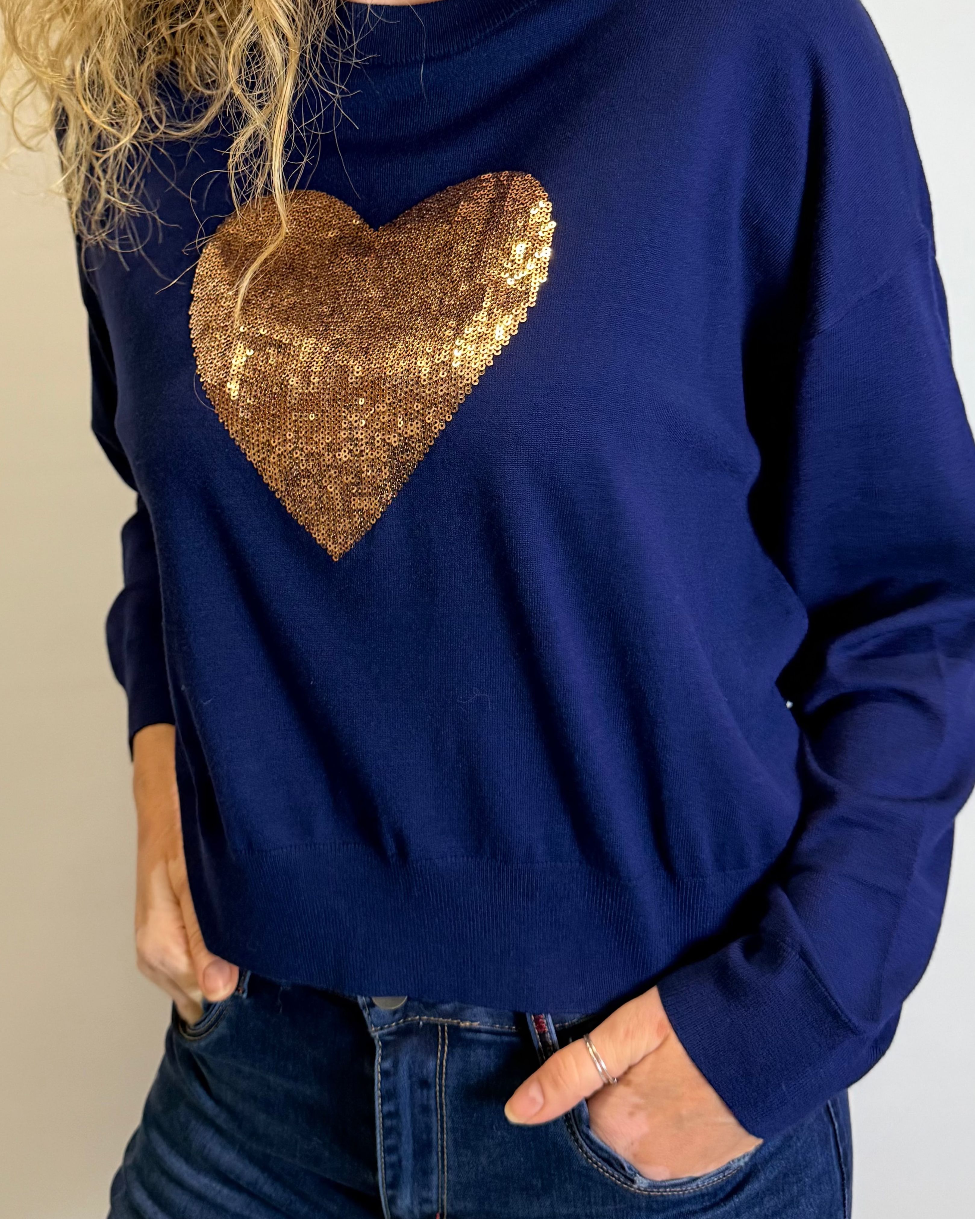 Woman wearing a blue sweater with a gold sequin heart design on a plain background