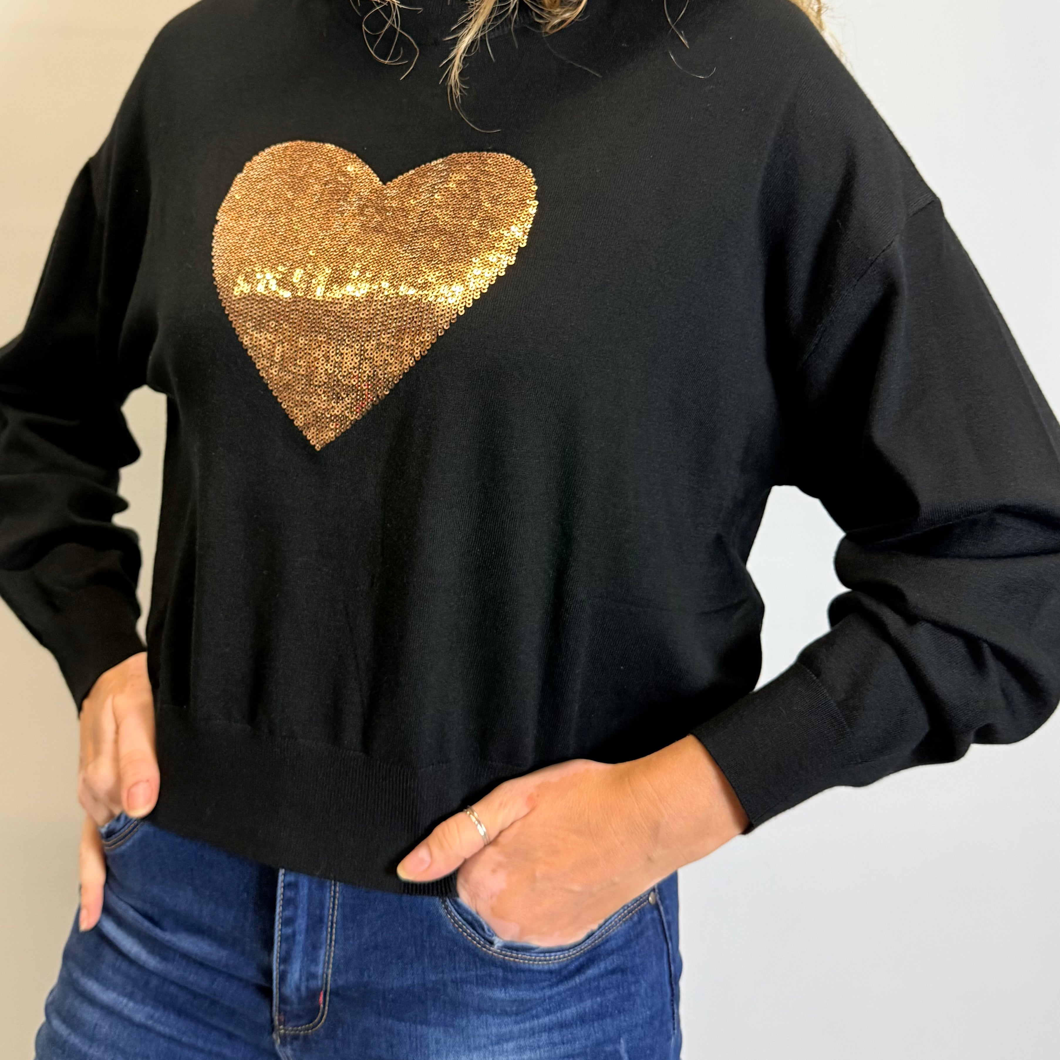 Person wearing a black sweatshirt with a gold sequin heart design.