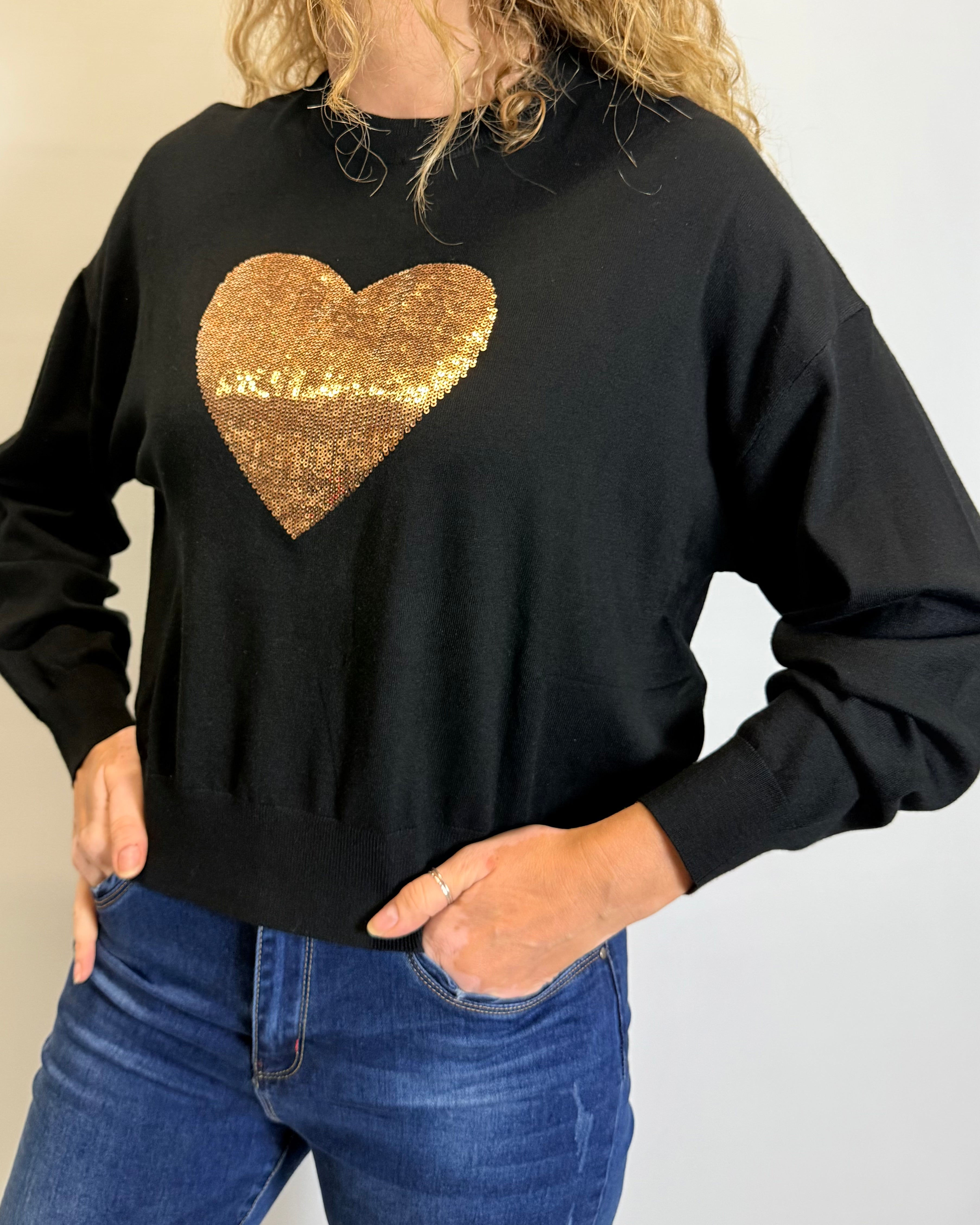 Person wearing a black sweatshirt with a gold sequin heart design.