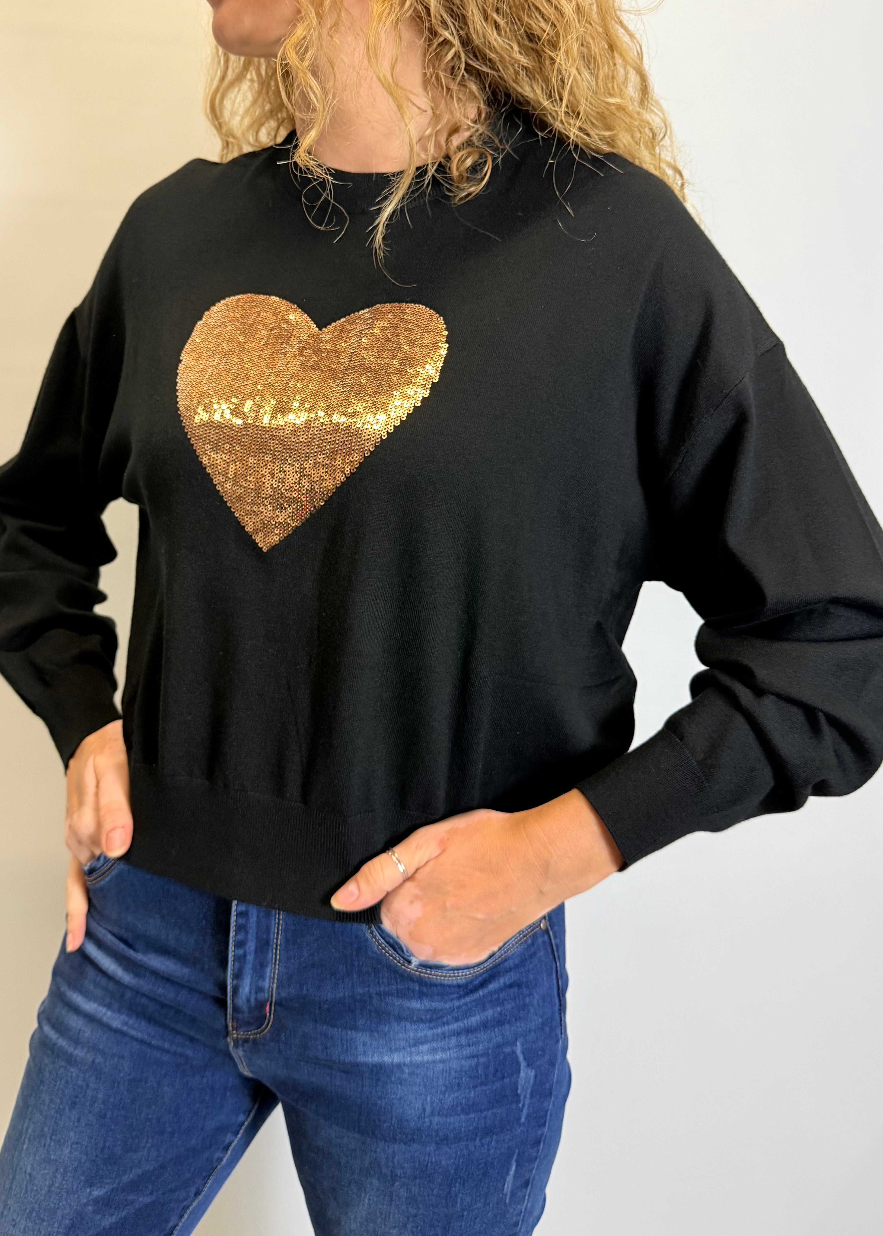 Person wearing a black sweatshirt with a gold sequin heart design.