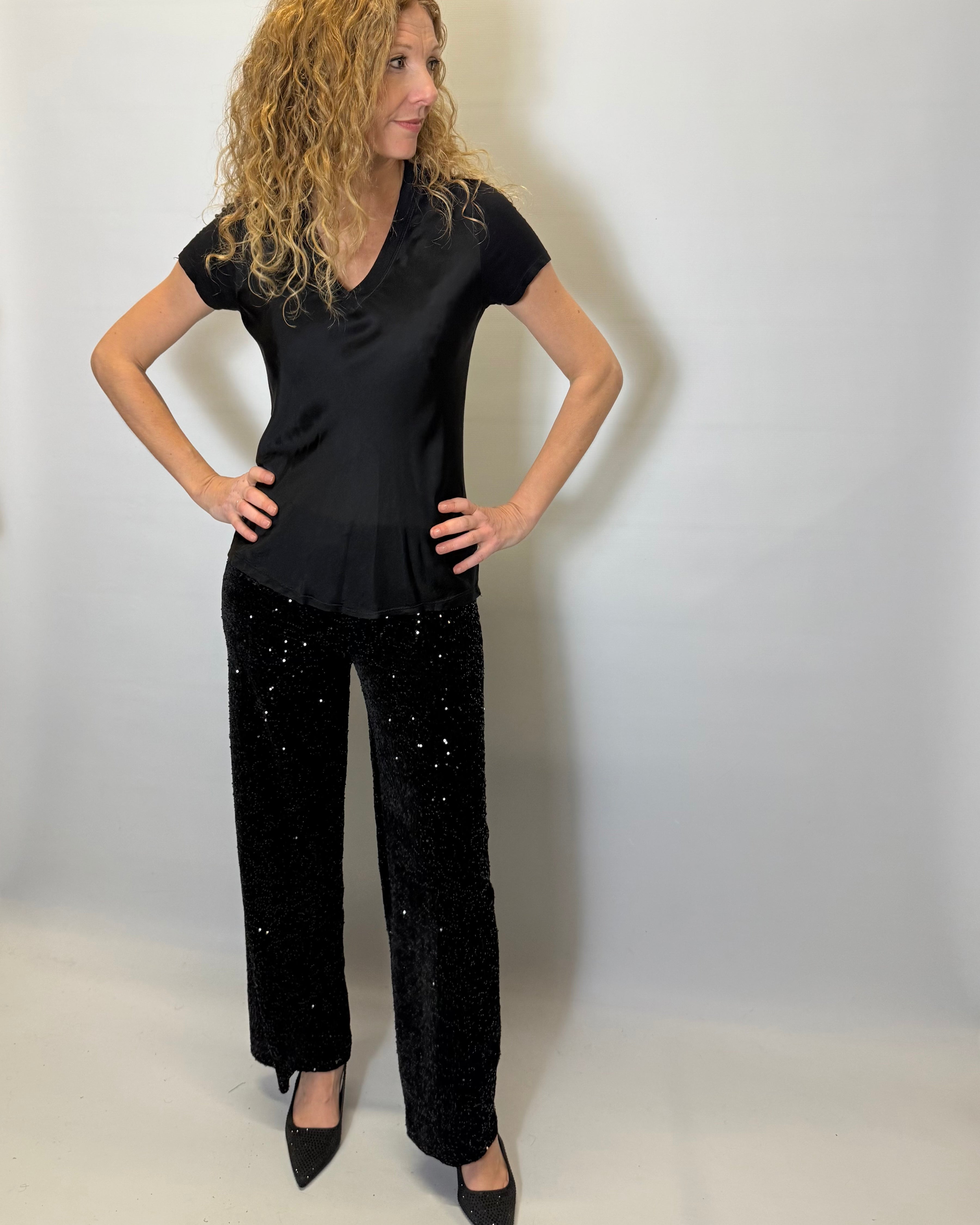 Woman wearing a black top and black pants with white speckles against a plain background