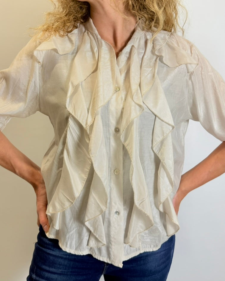 Woman wearing a white blouse with ruffled details against a neutral background