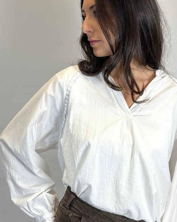 Woman wearing a white blouse with rolled-up sleeves against a plain background