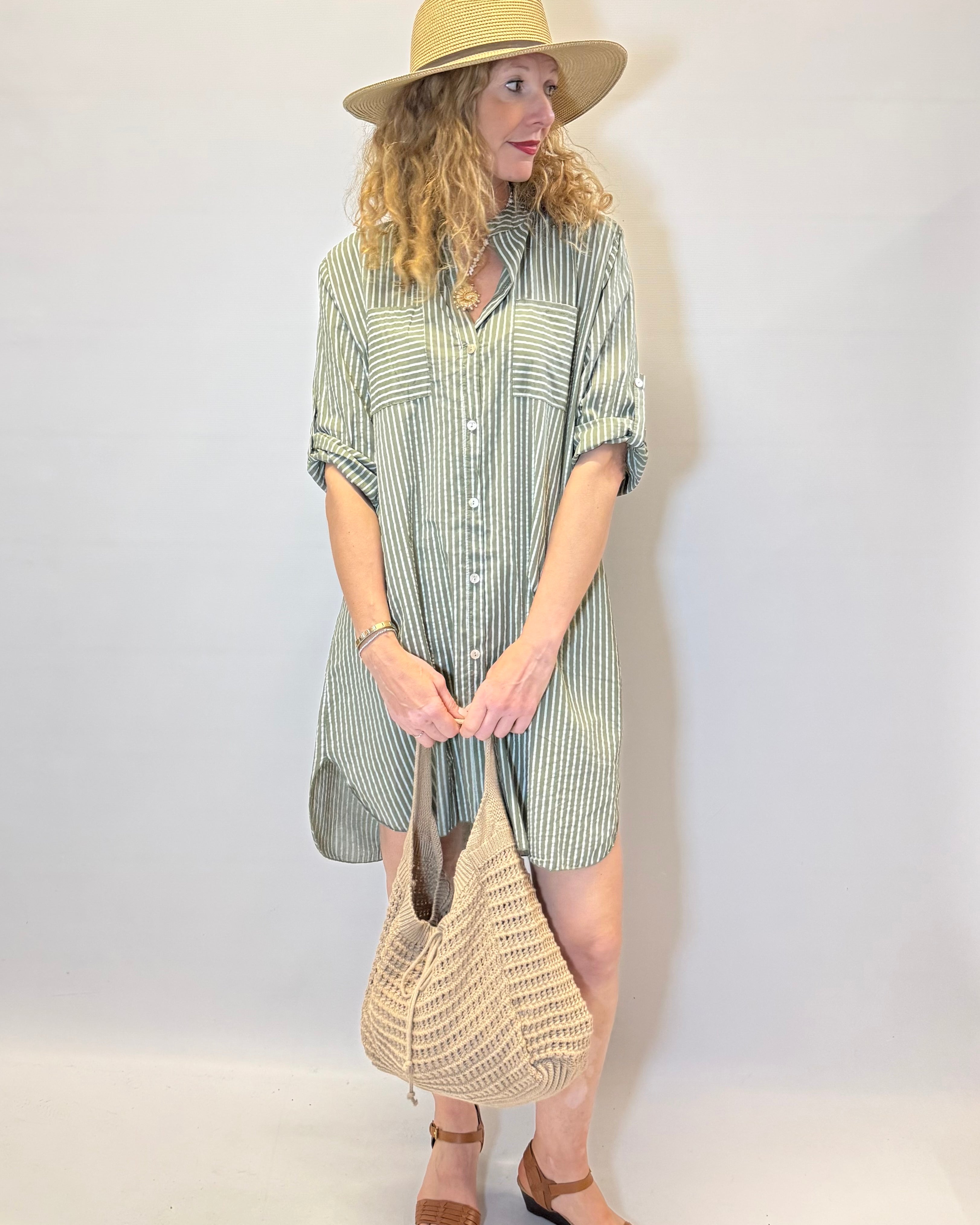 Woman wearing a striped dress and hat, holding a bag against a white background