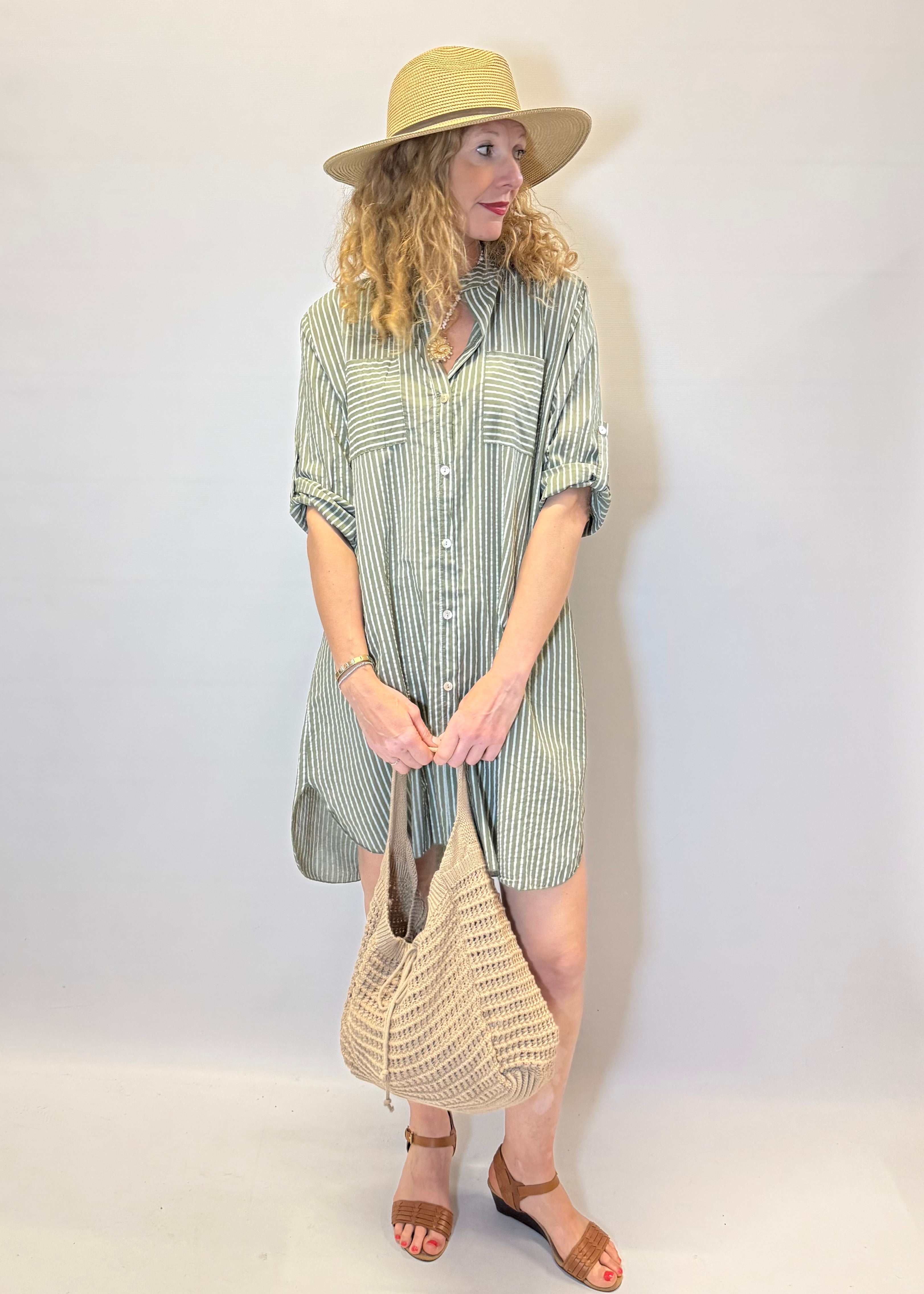 Woman wearing a striped dress and hat, holding a bag against a white background