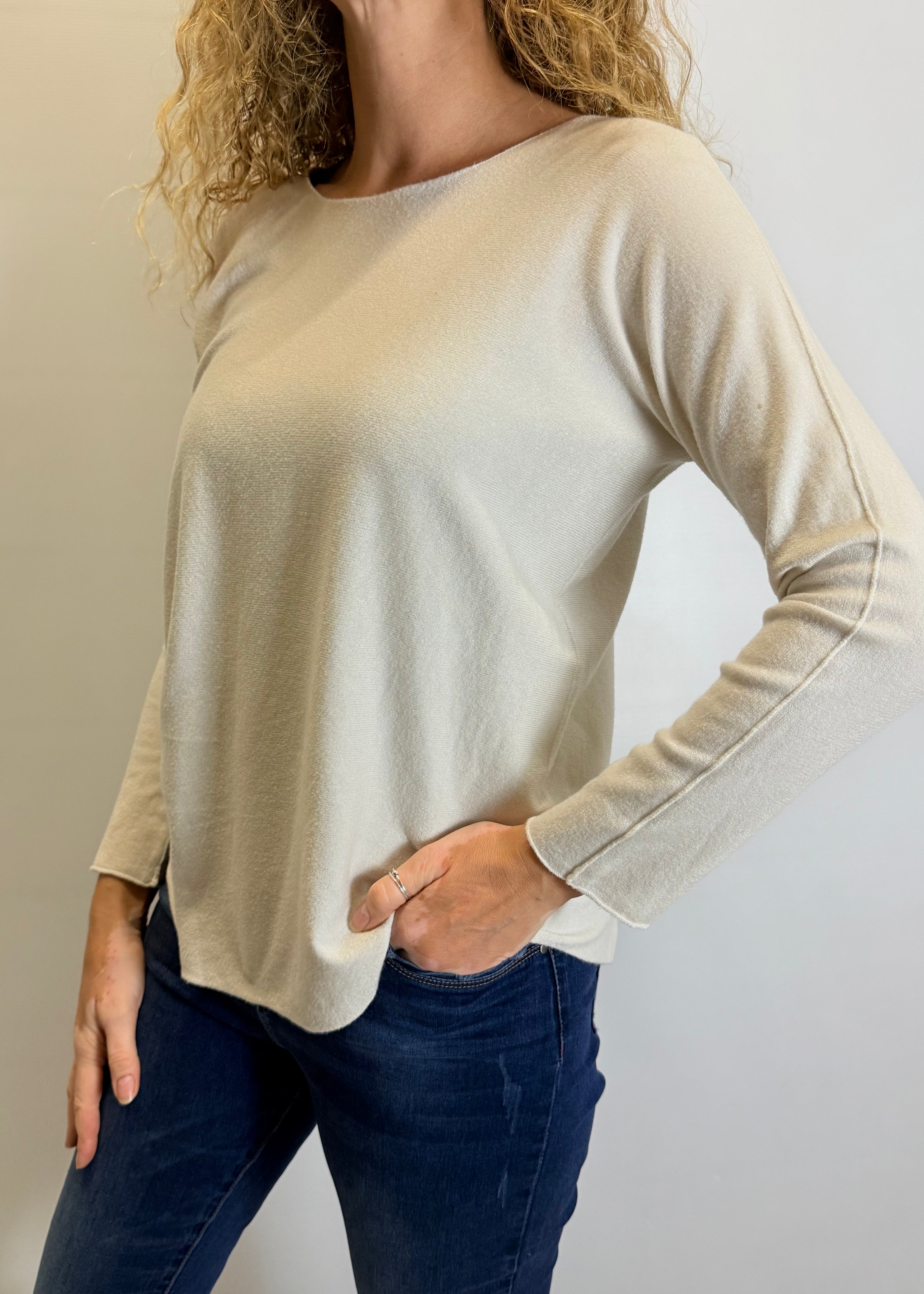 Woman wearing a beige long-sleeve top and dark blue jeans against a plain background