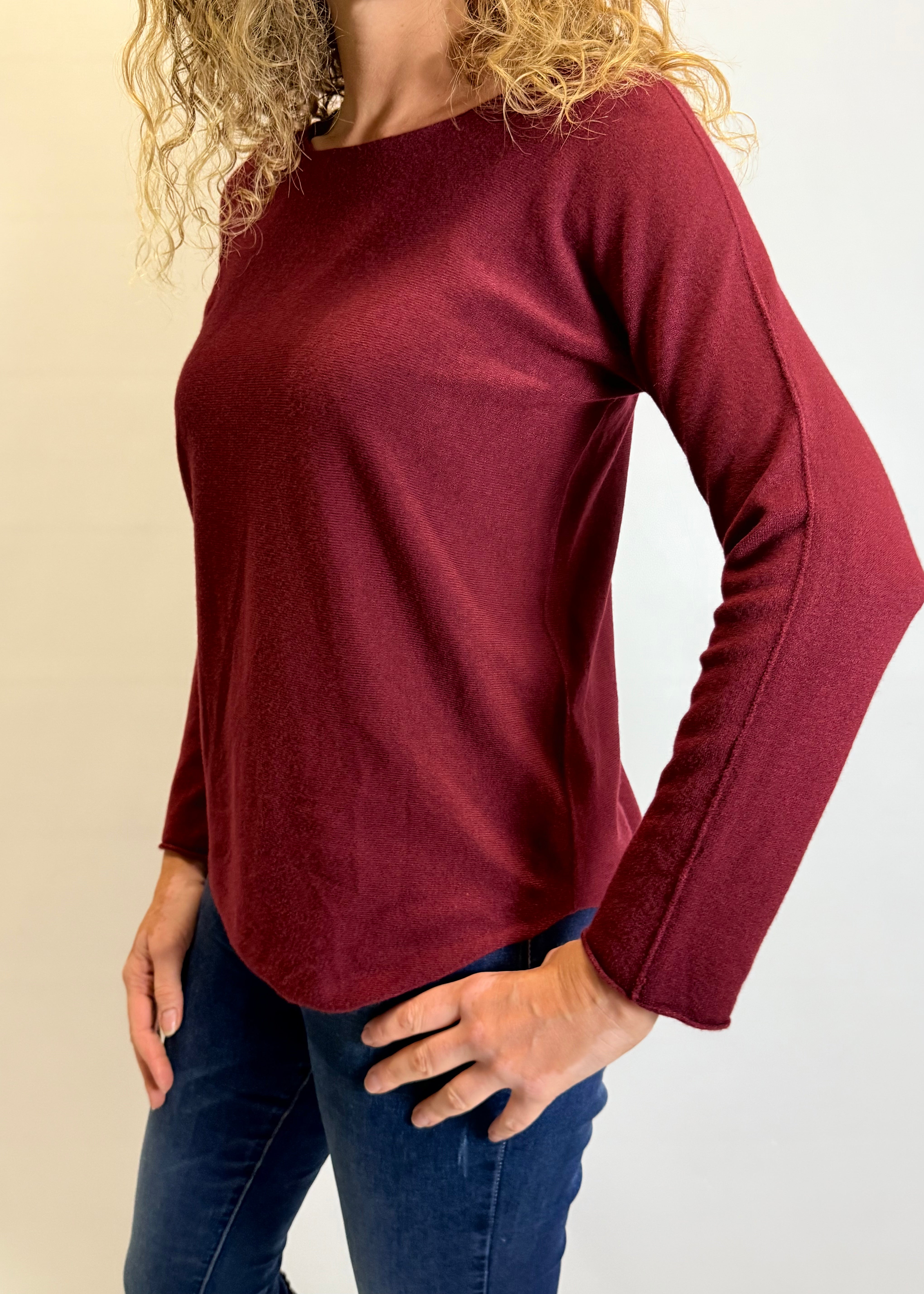 Person wearing a burgundy long-sleeve top and blue jeans on a plain background