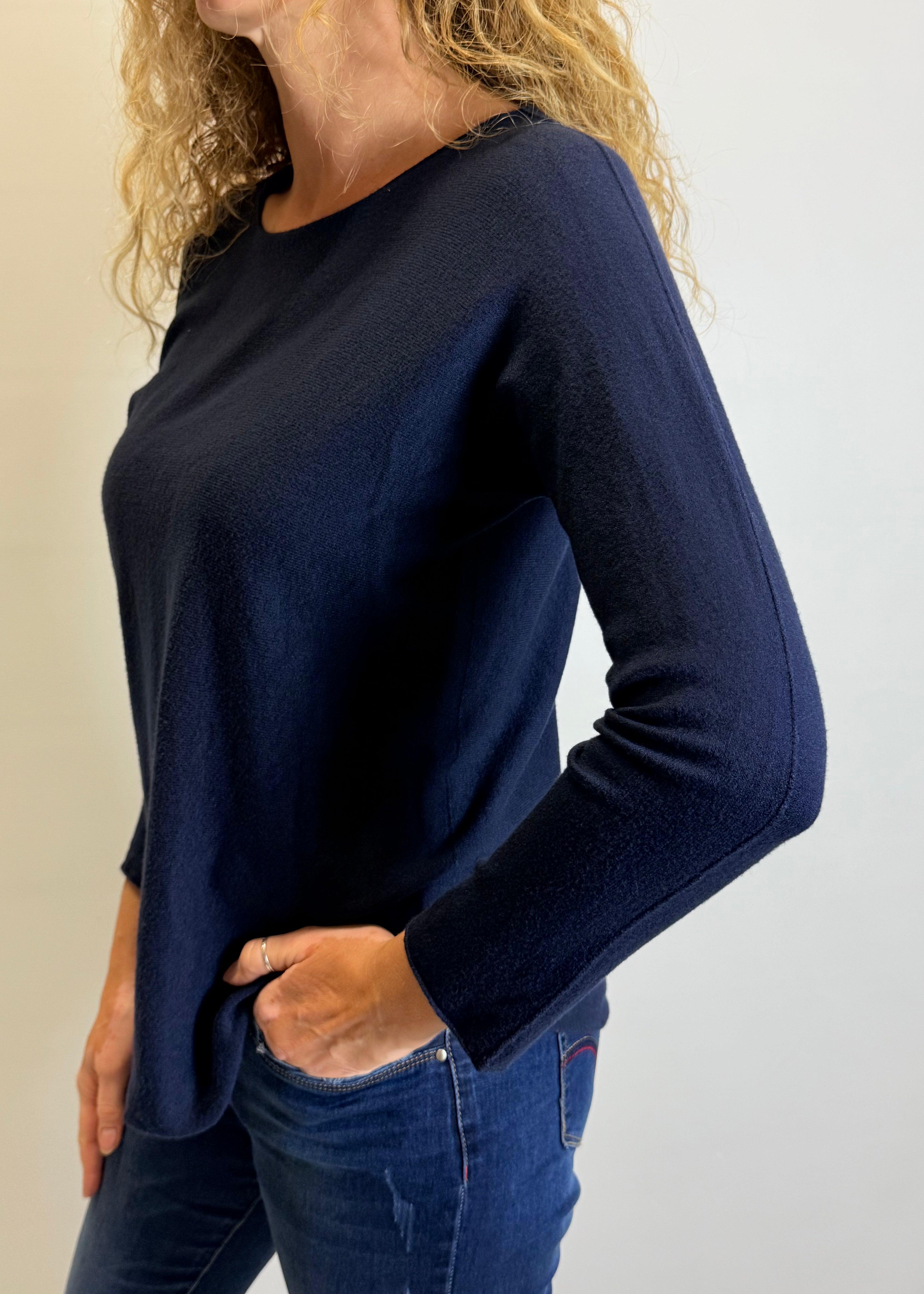 Person wearing a navy blue sweater and jeans against a plain background