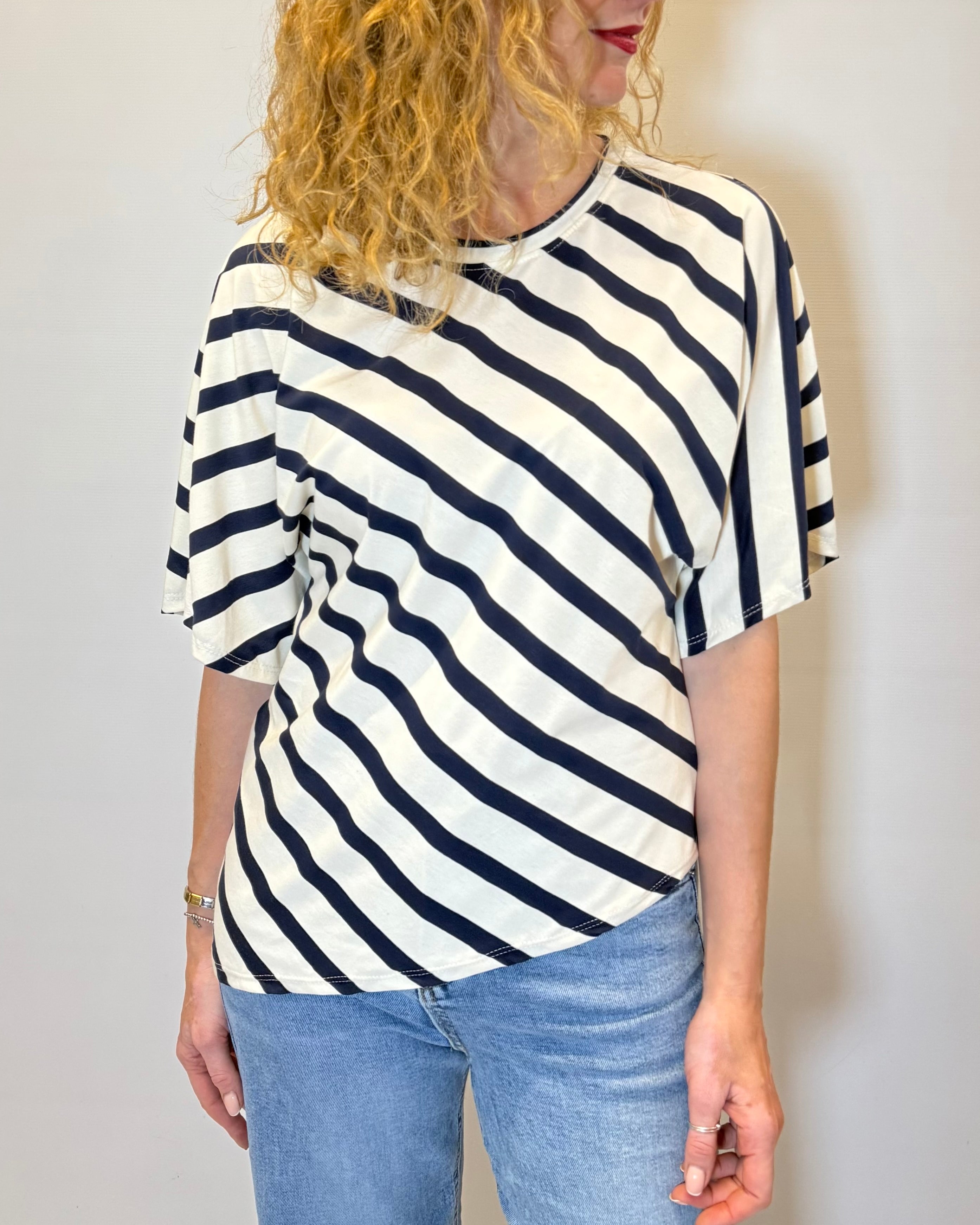 Person wearing a black and white striped shirt with blue jeans against a plain background