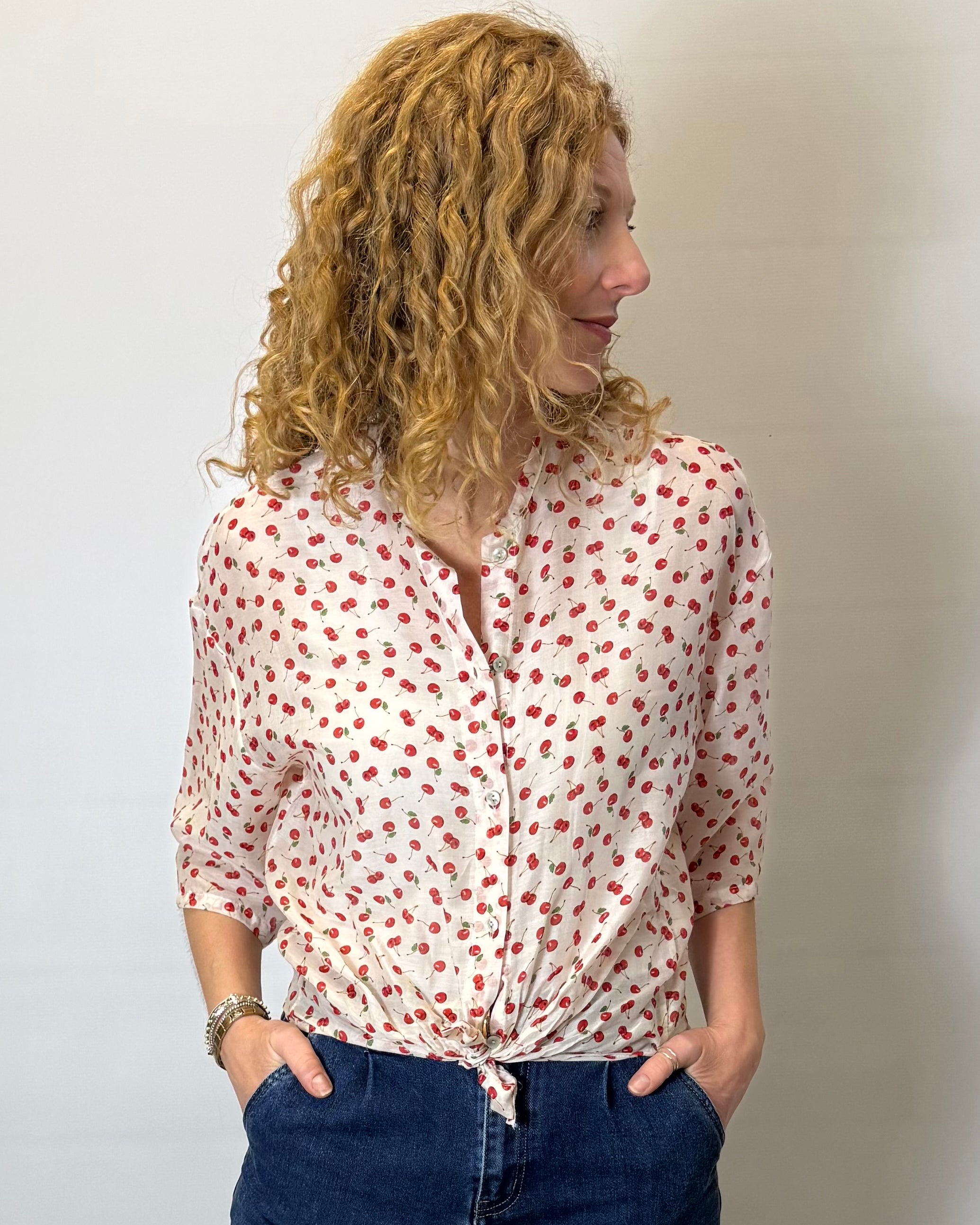 Woman wearing a white blouse with red patterns and blue jeans against a plain background