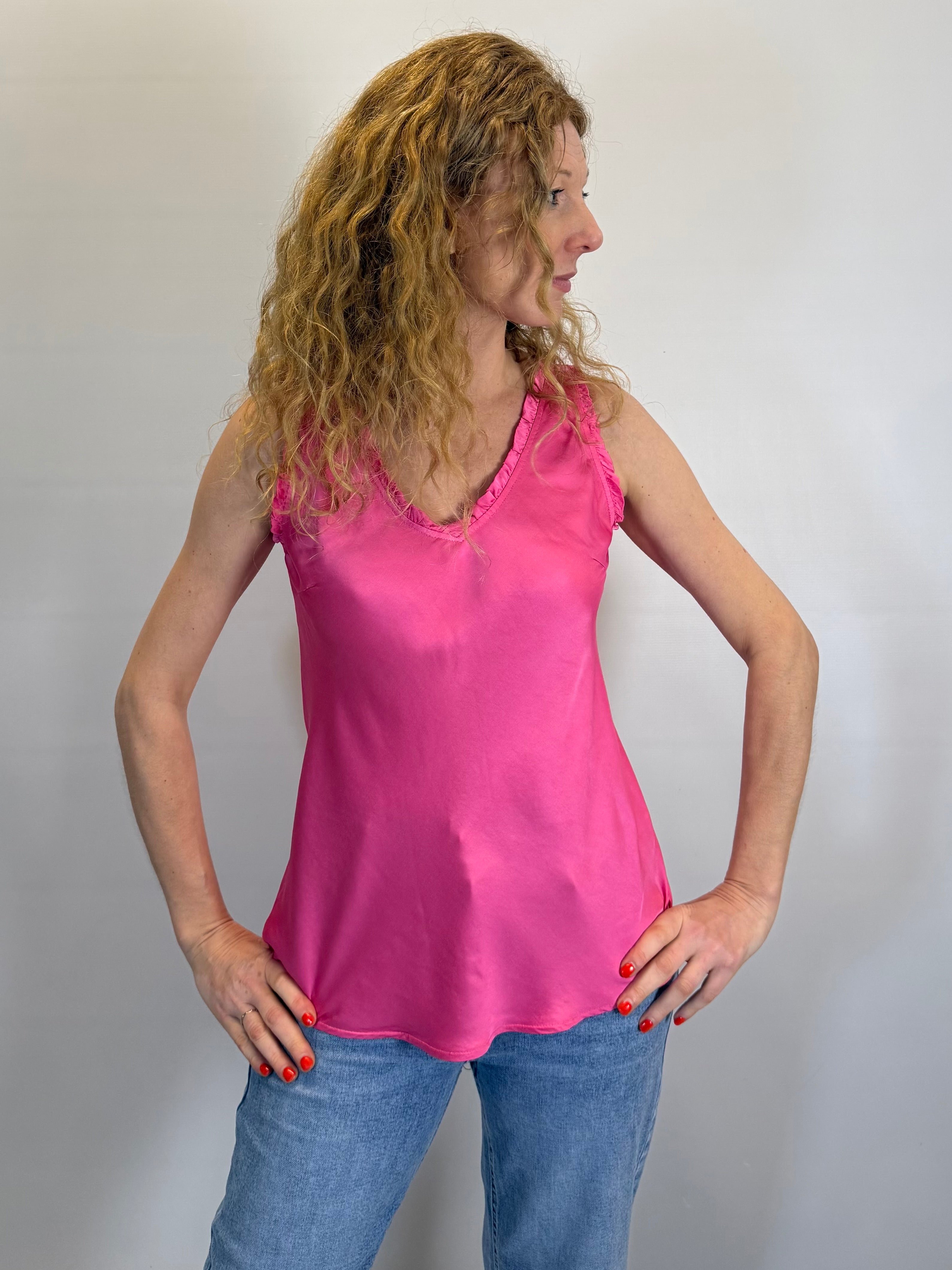 Woman wearing a pink sleeveless top and blue jeans against a plain background