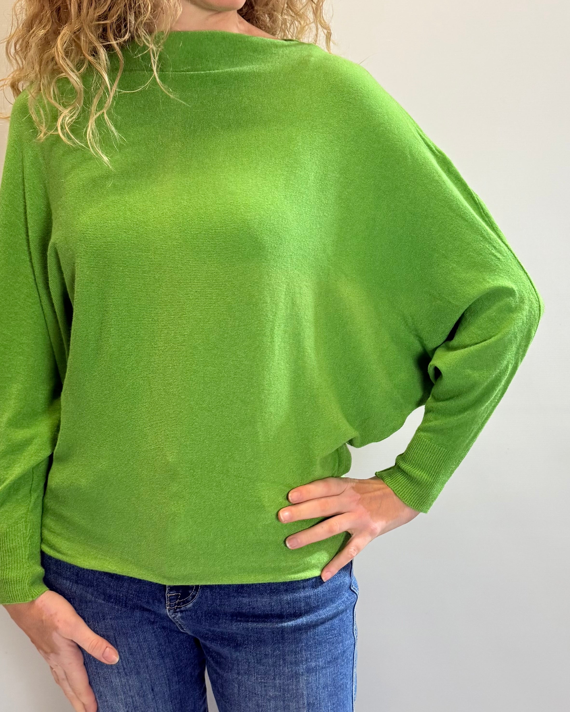 Person wearing a green long-sleeve top and blue jeans against a plain background