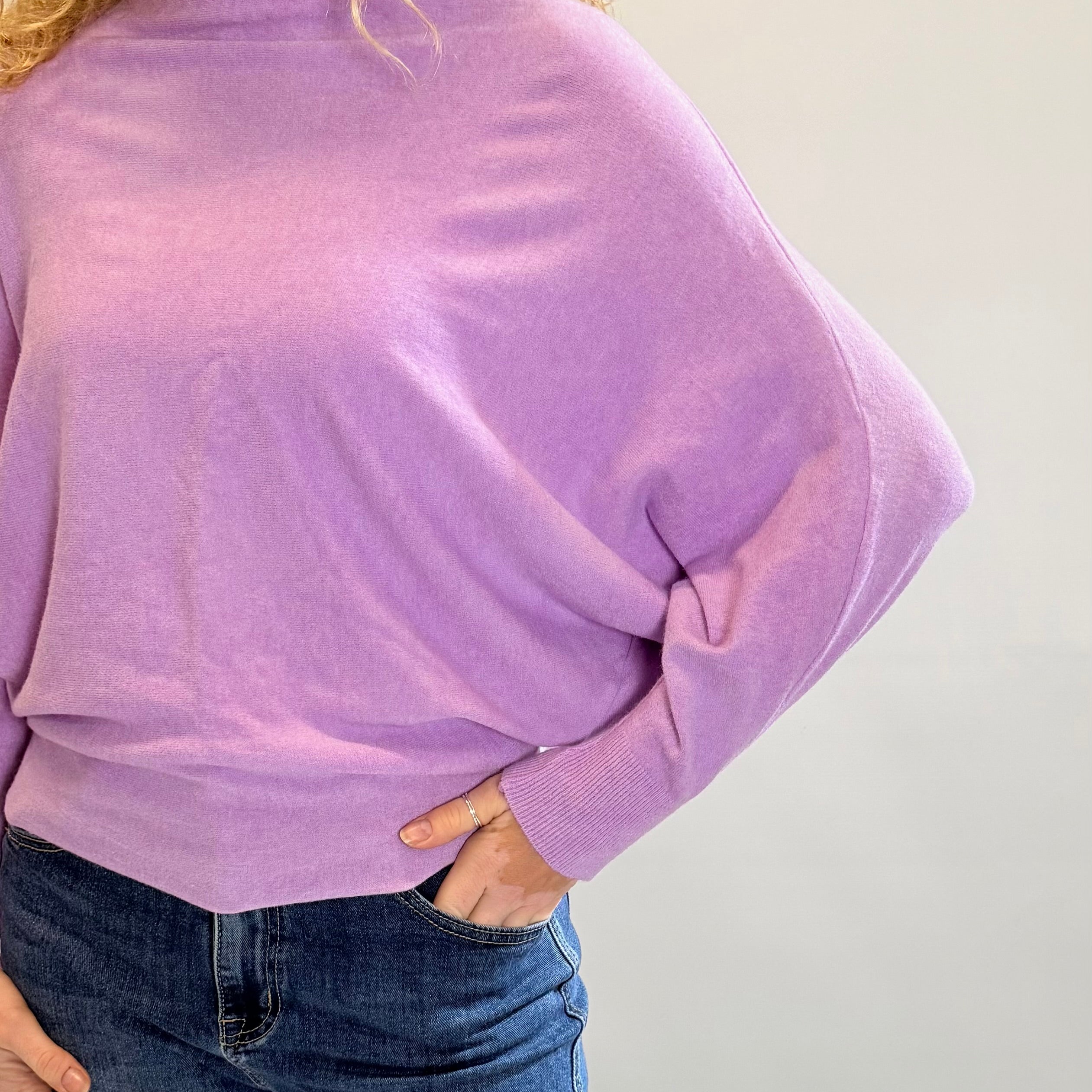 Person wearing a purple sweater and blue jeans against a plain background