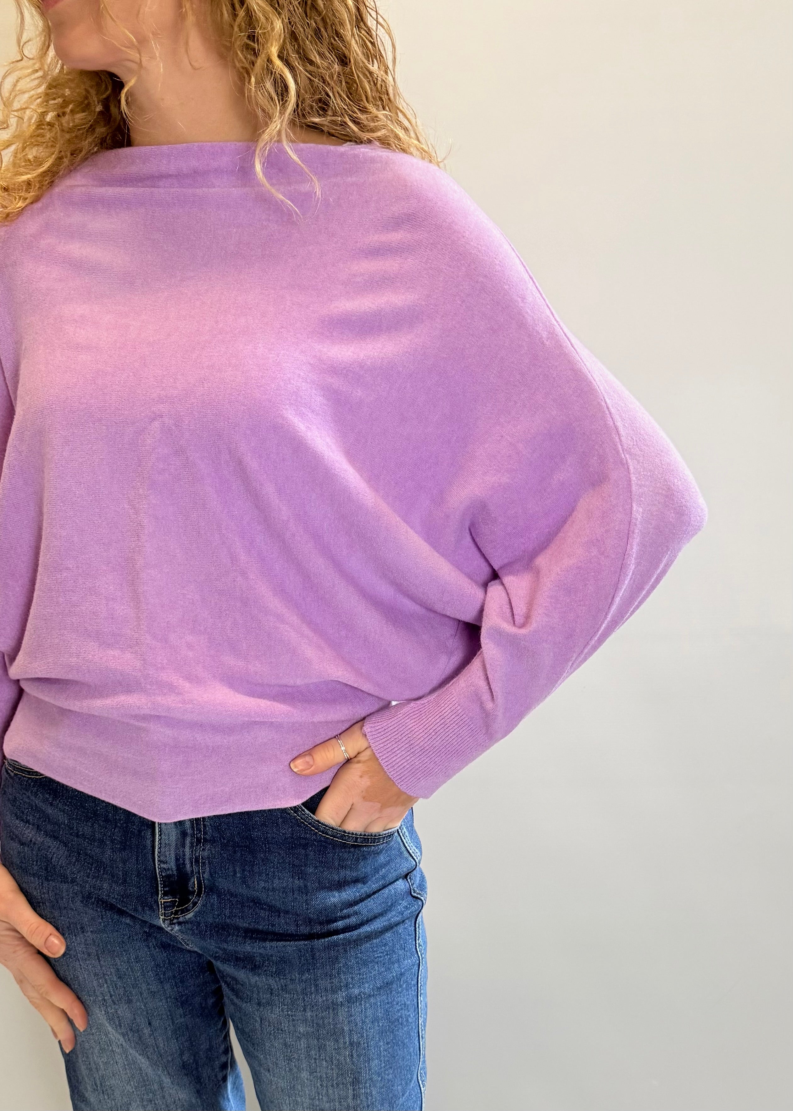 Person wearing a purple sweater and blue jeans against a plain background
