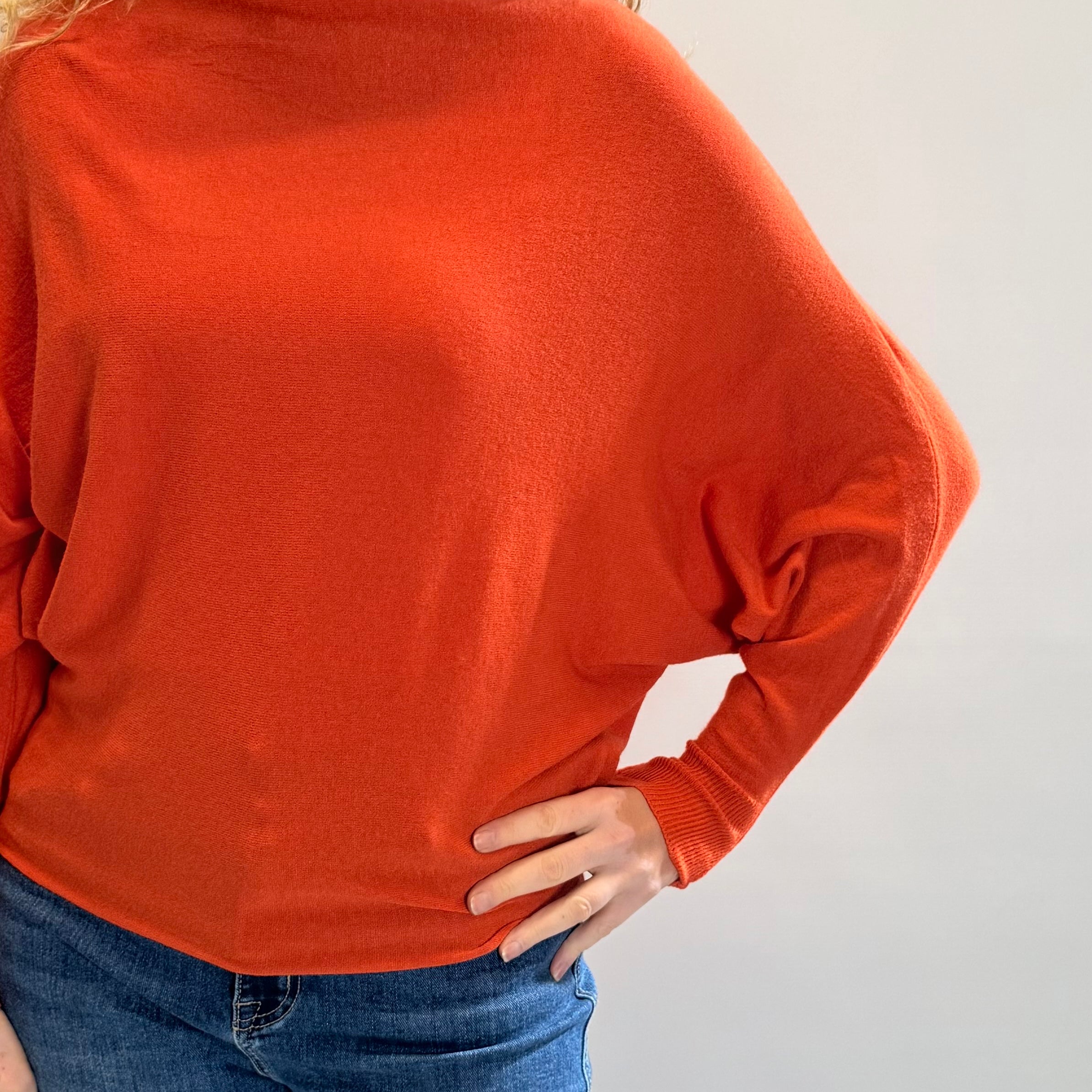 Person wearing an orange sweater and blue jeans against a plain background