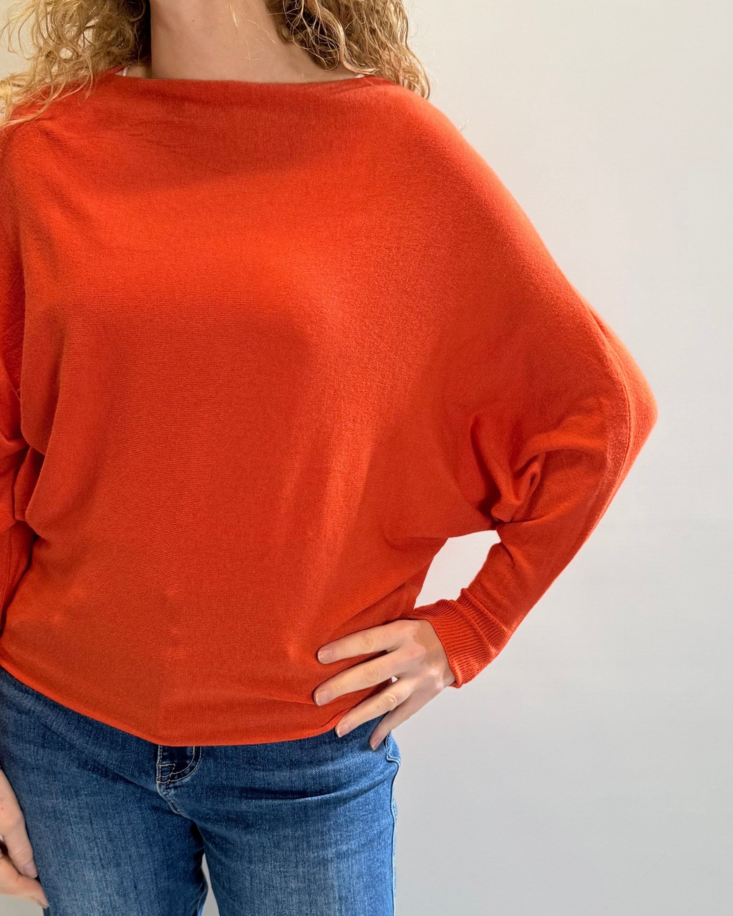 Person wearing an orange sweater and blue jeans against a plain background