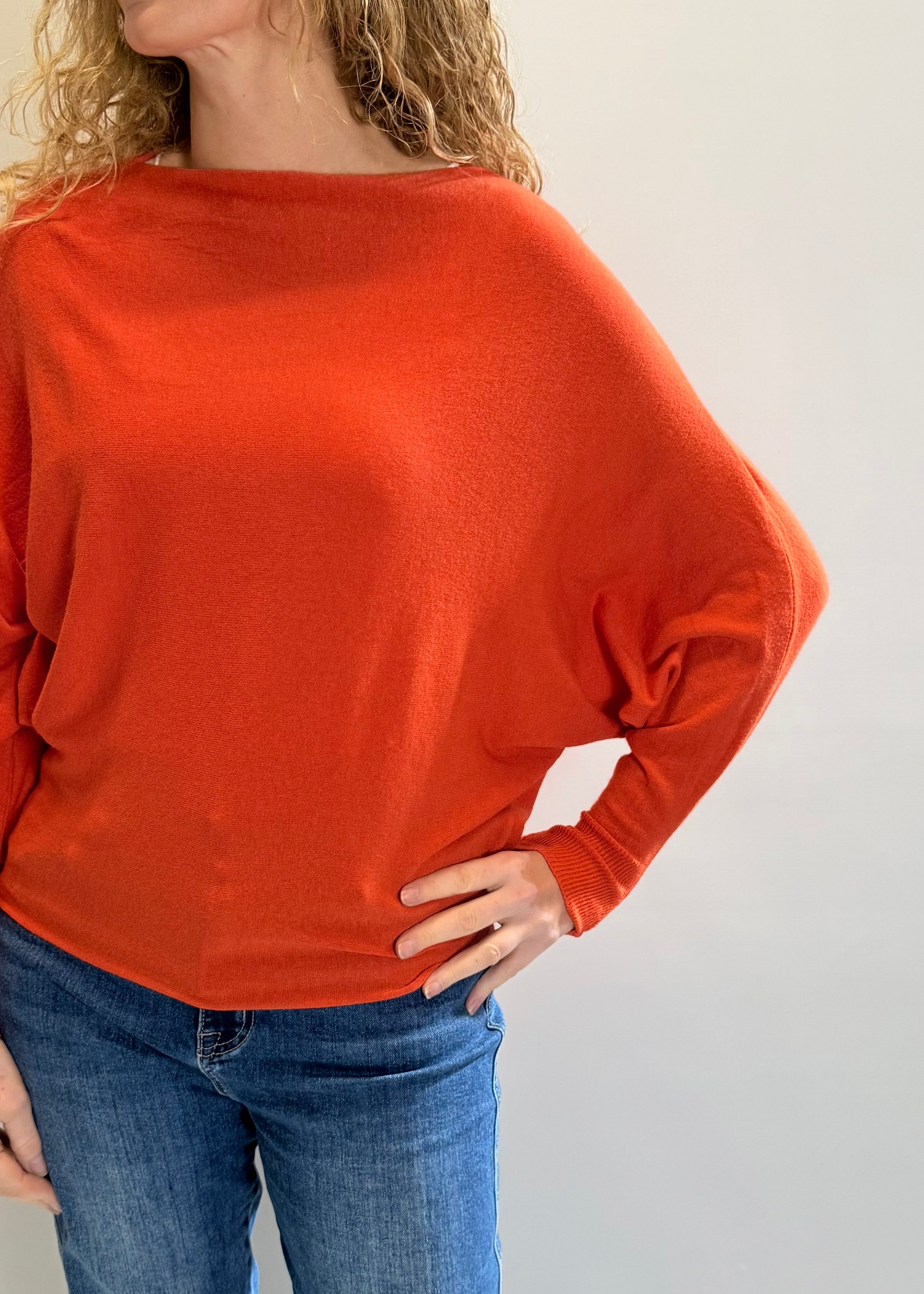 Person wearing an orange sweater and blue jeans against a plain background