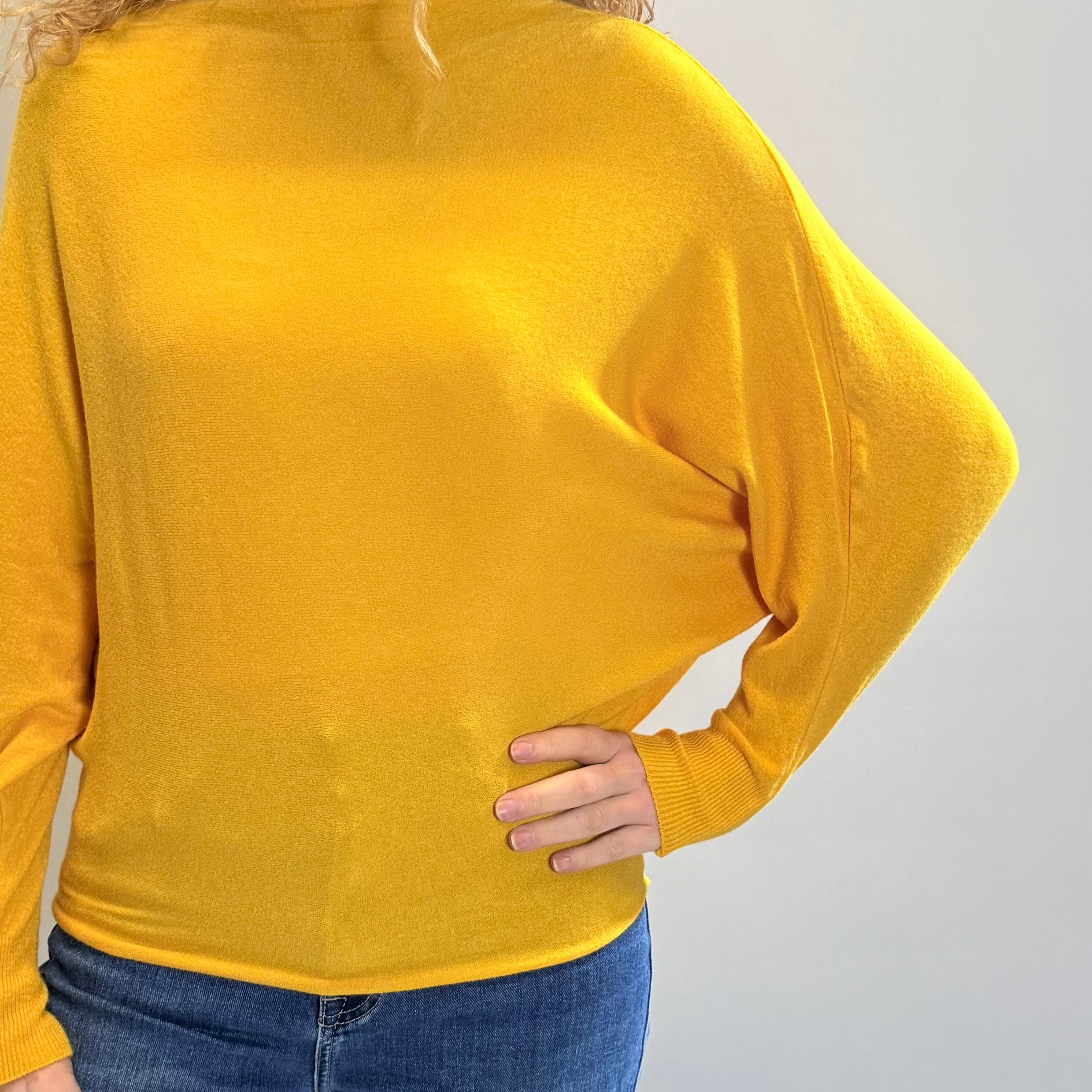 Person wearing a yellow sweater and blue jeans on a plain background