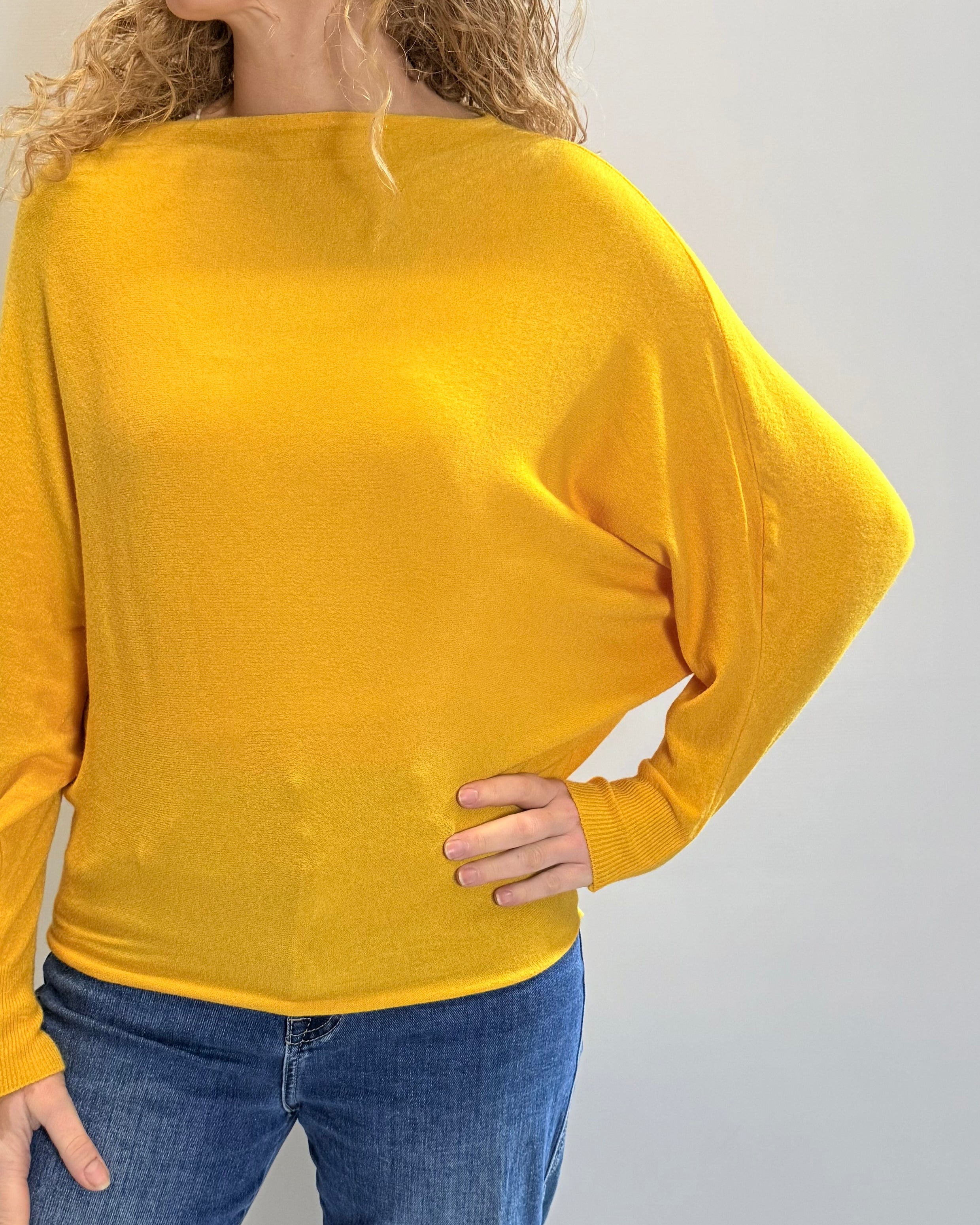 Person wearing a yellow sweater and blue jeans on a plain background