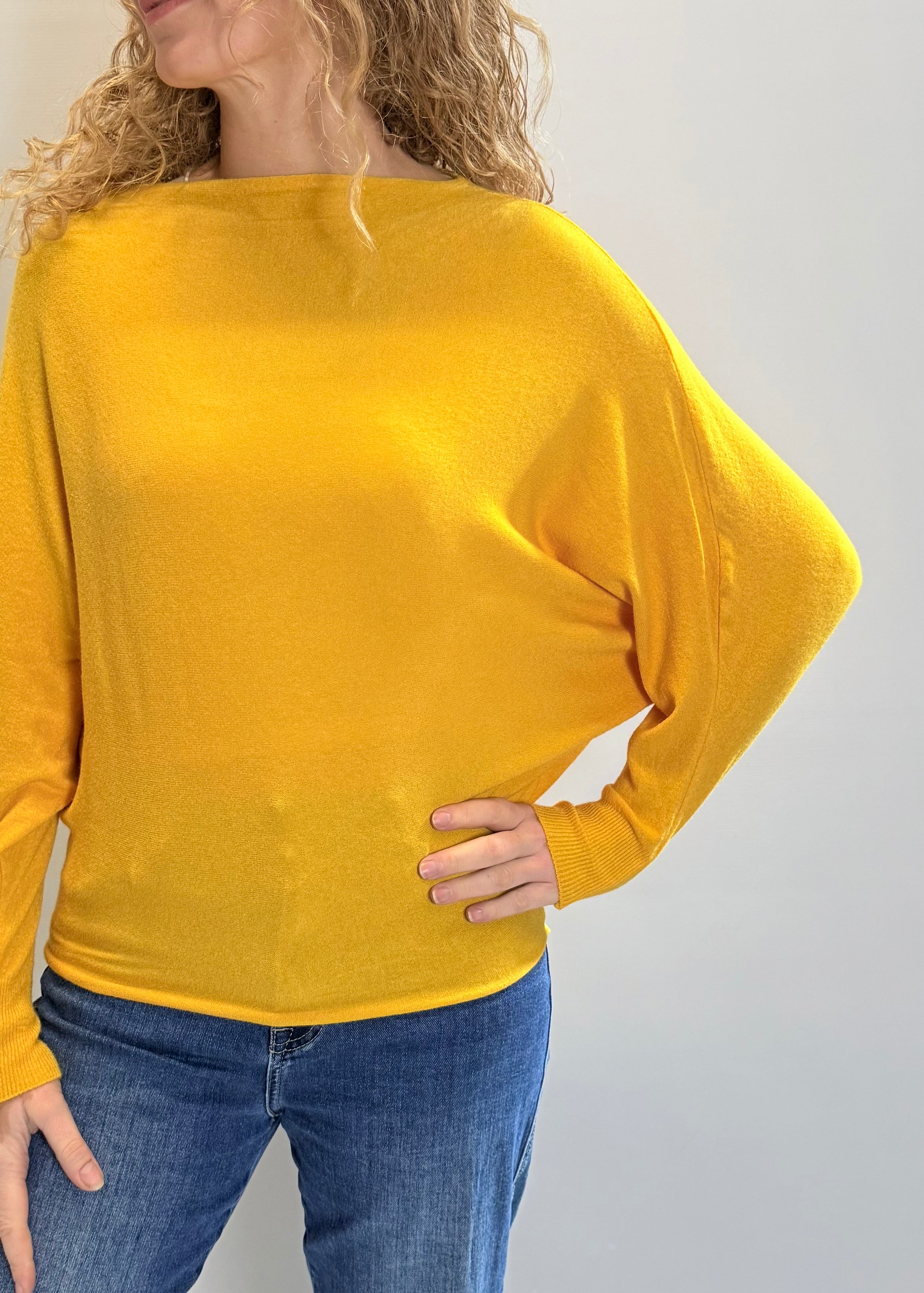 Person wearing a yellow sweater and blue jeans on a plain background