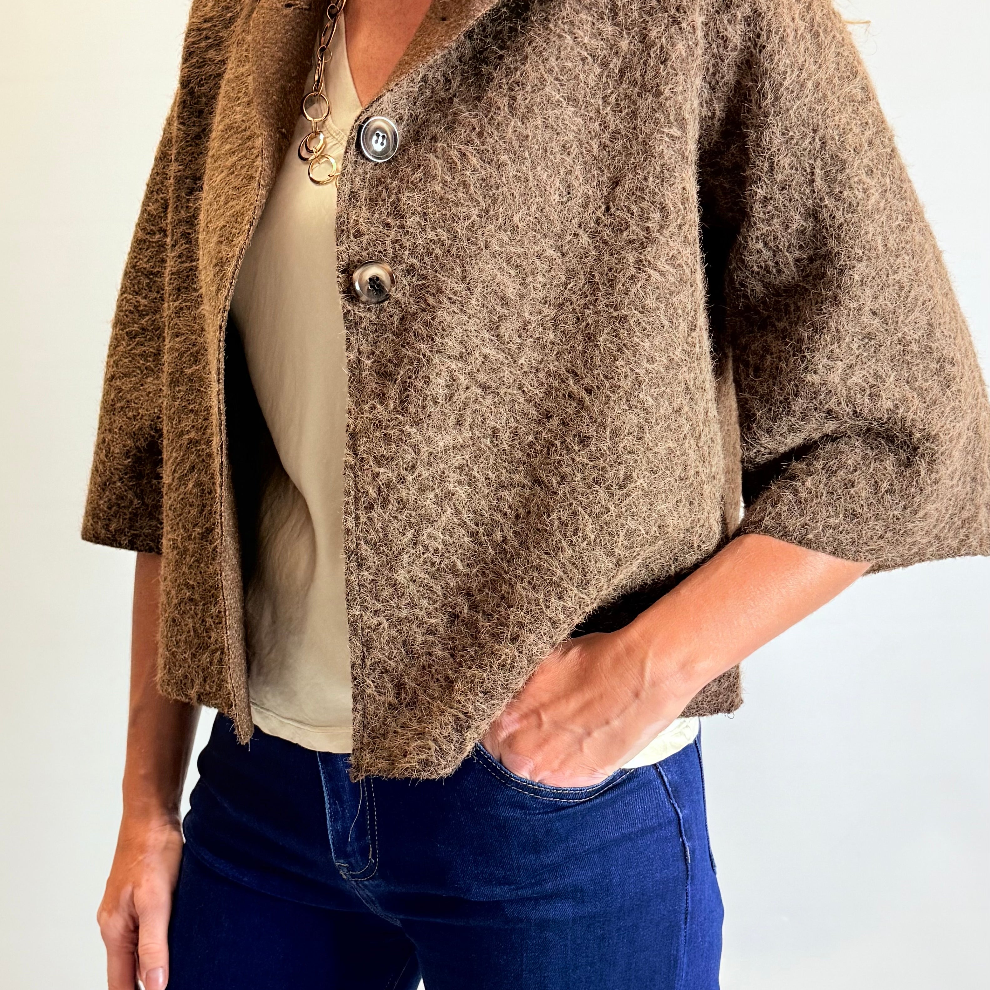 Person wearing a brown textured jacket over a white shirt and blue jeans on a plain background