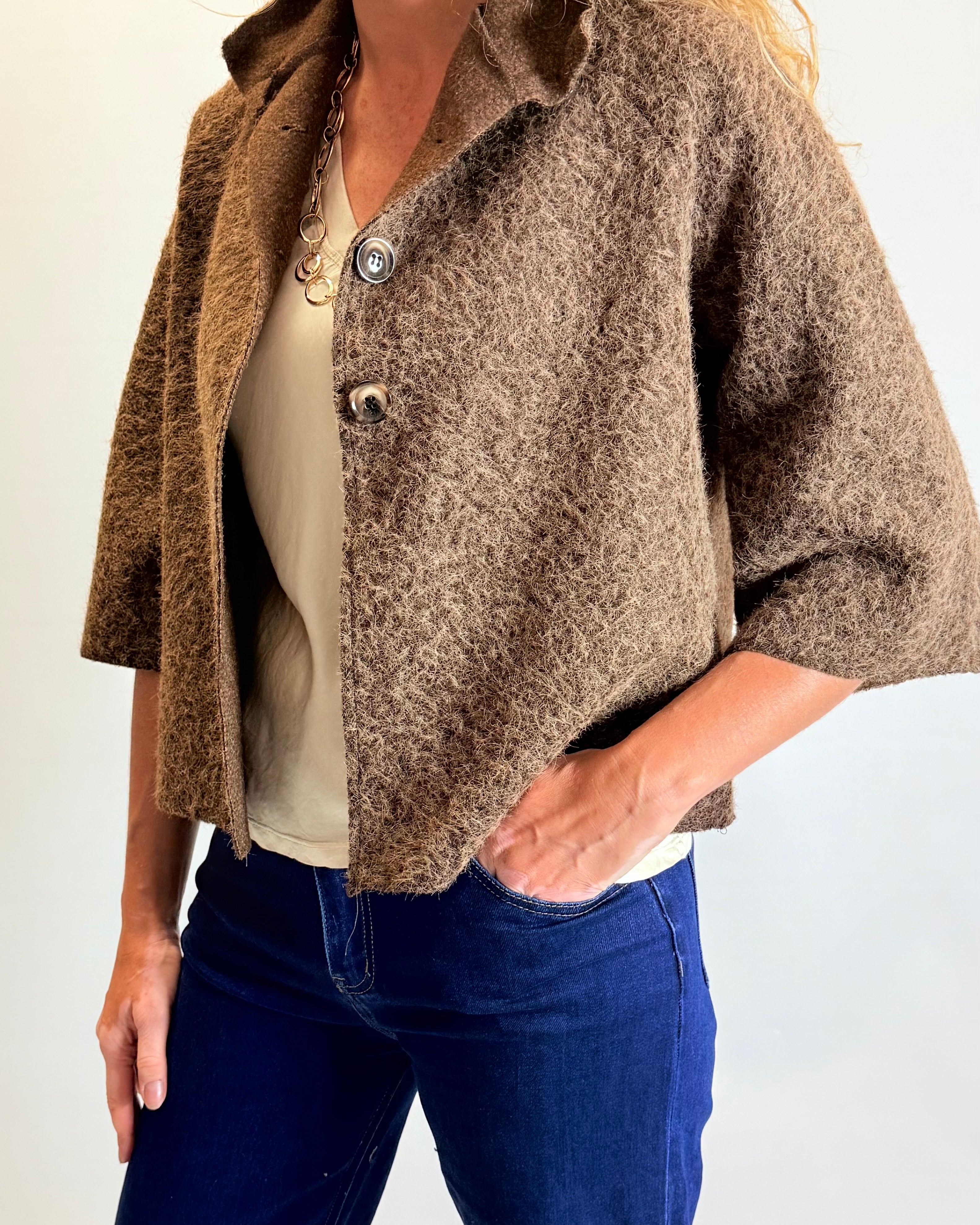 Person wearing a brown textured jacket over a white shirt and blue jeans on a plain background