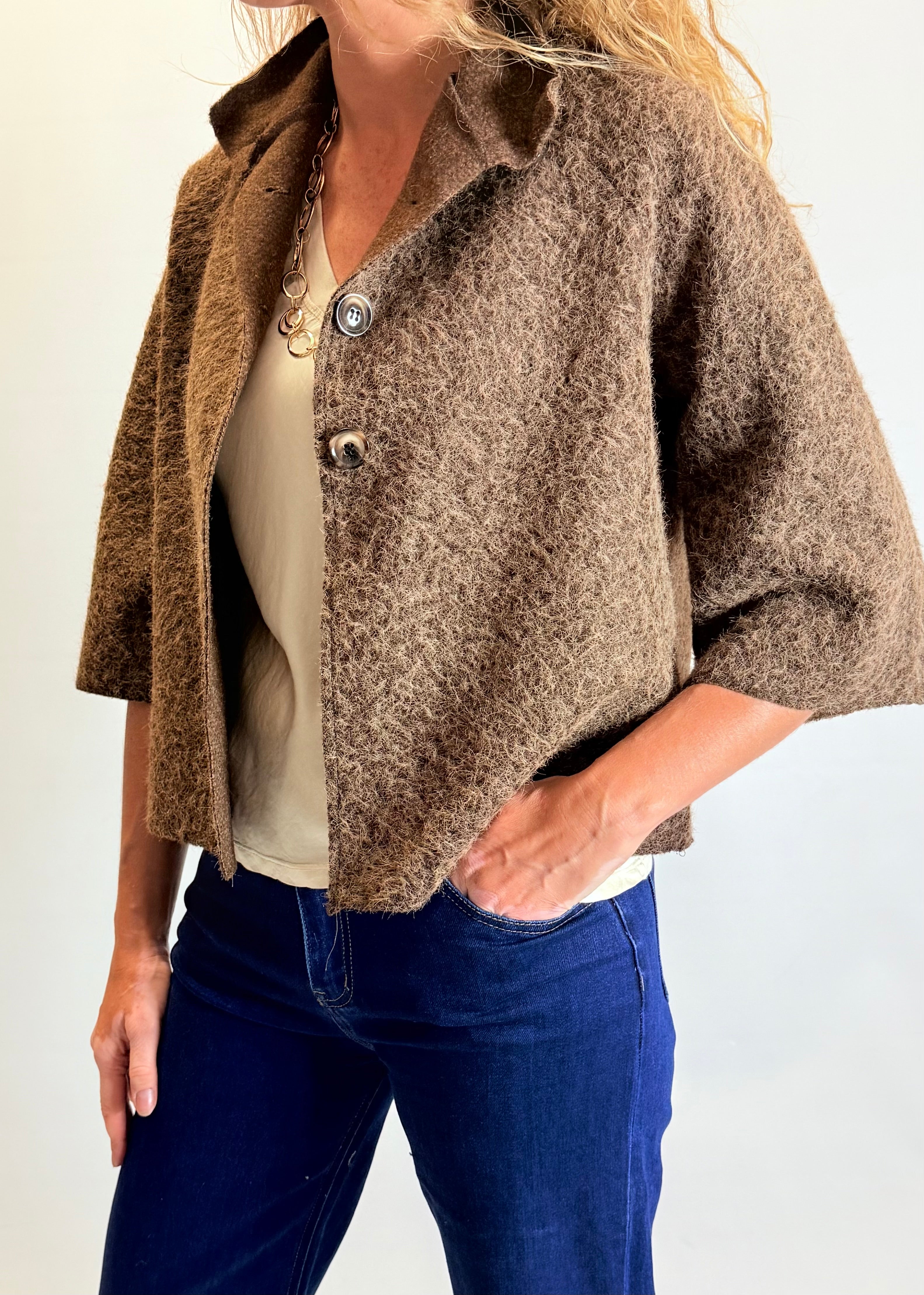 Person wearing a brown textured jacket over a white shirt and blue jeans on a plain background