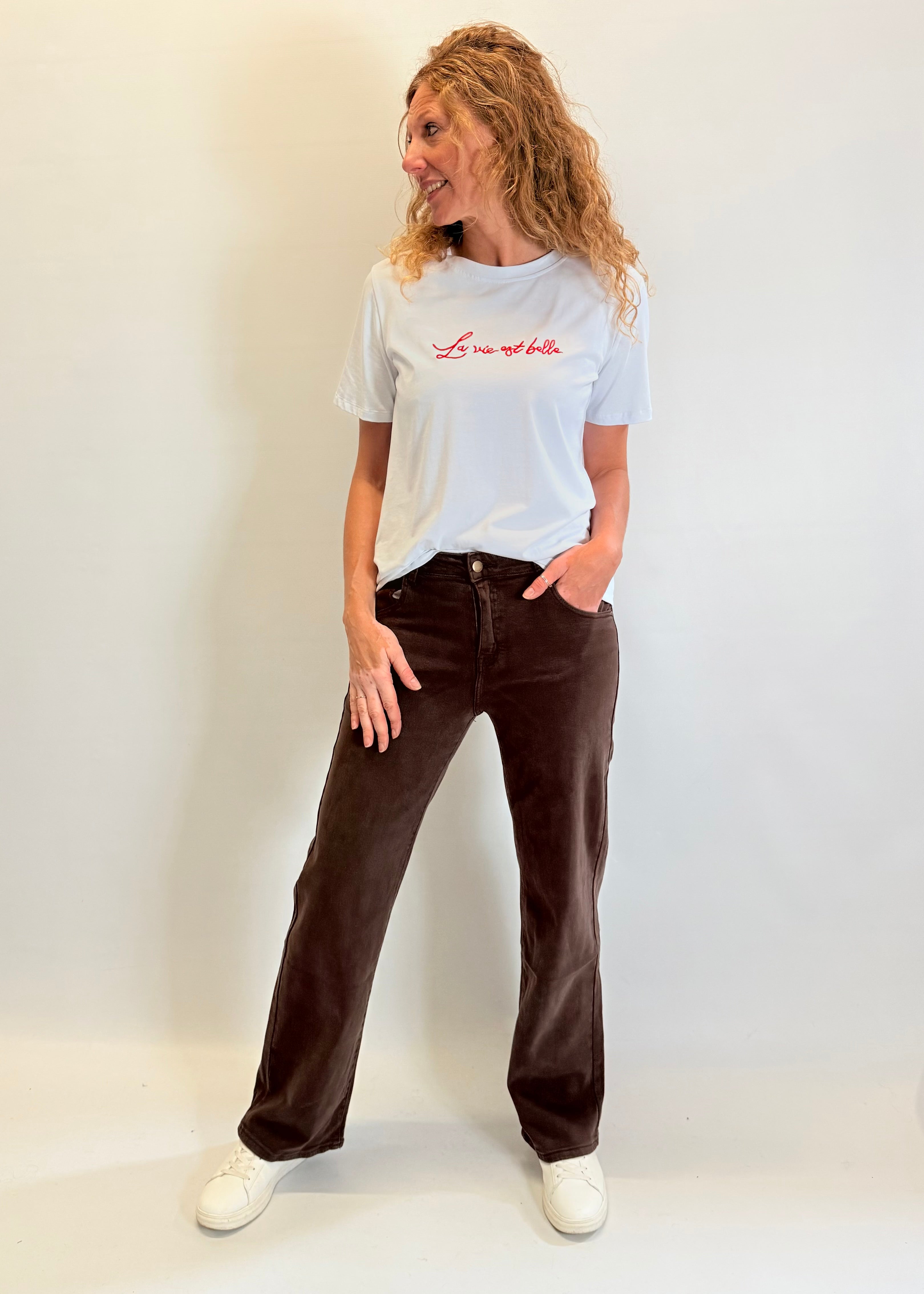 Person wearing a white t-shirt with text and brown pants against a plain background