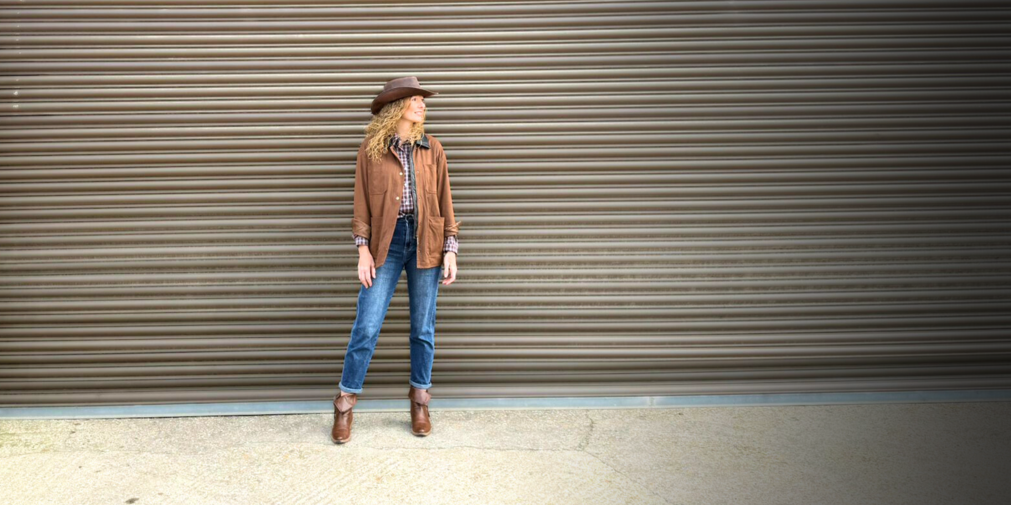 Woman wearing country clothing style with brown jacket, check shirt and jeans available in ladies boutique in Hampshire.