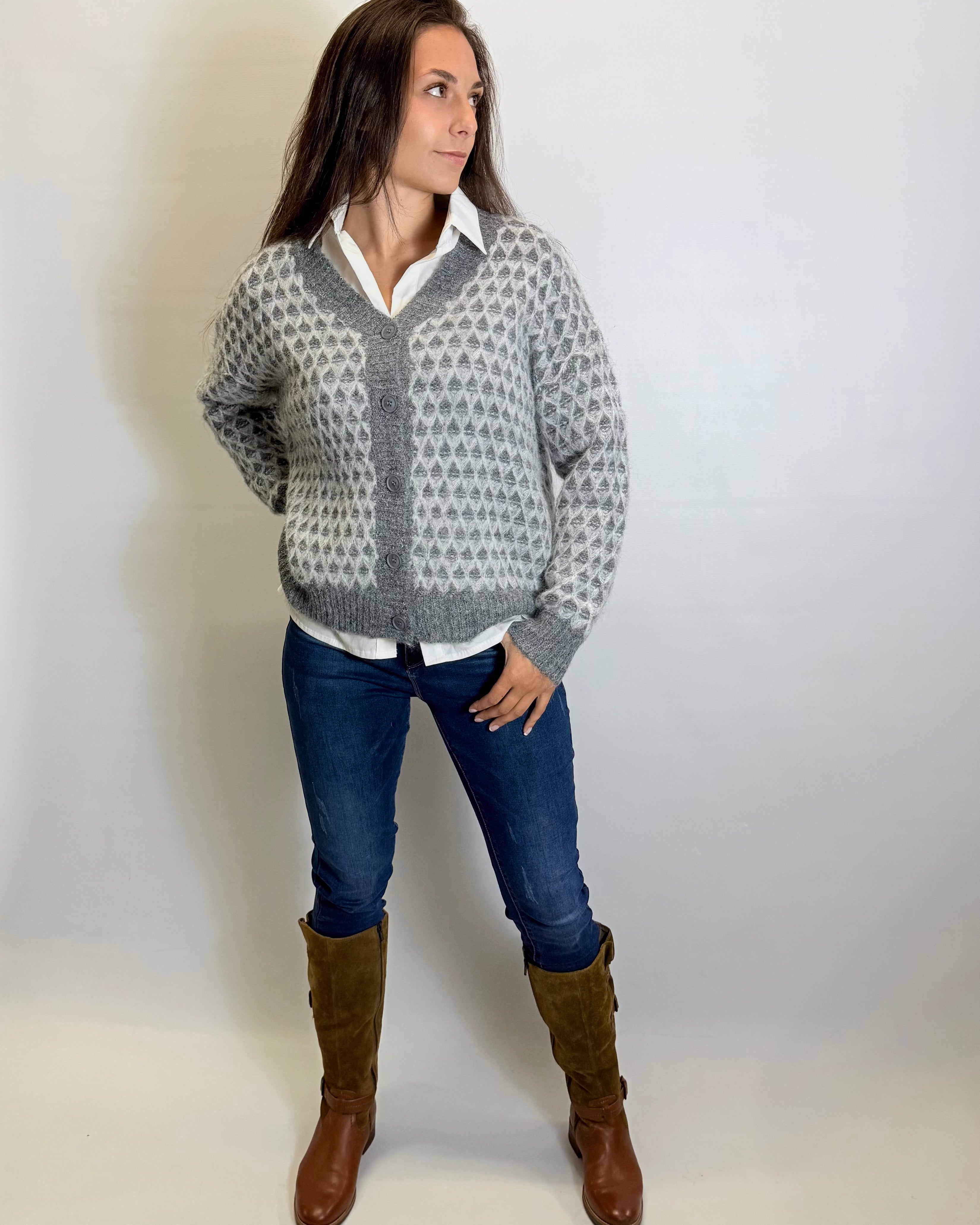 Woman wearing a patterned sweater, white shirt, blue jeans, and brown boots against a plain background