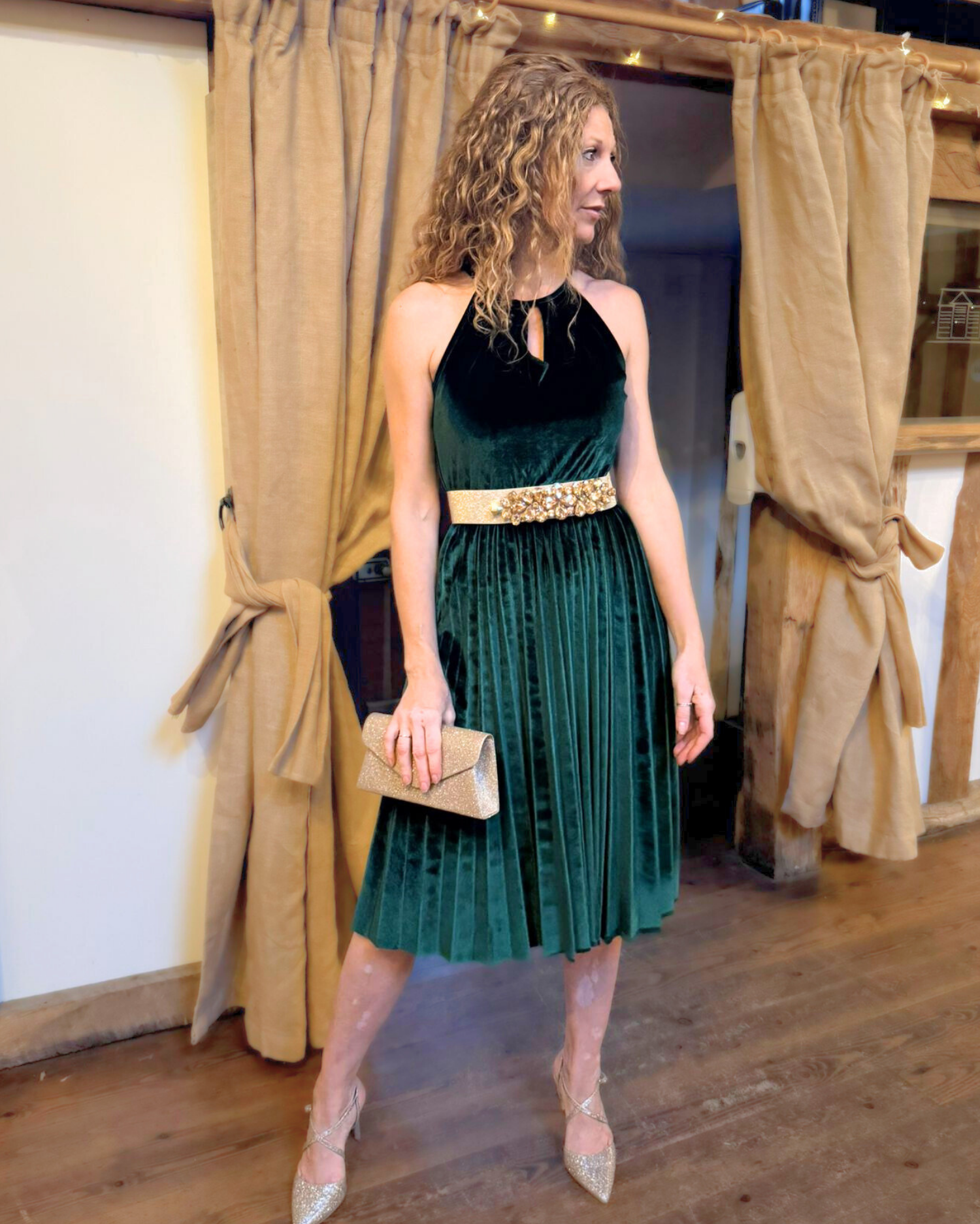 Lady wearing green velvet dress with gold belt and gold clutch bag.