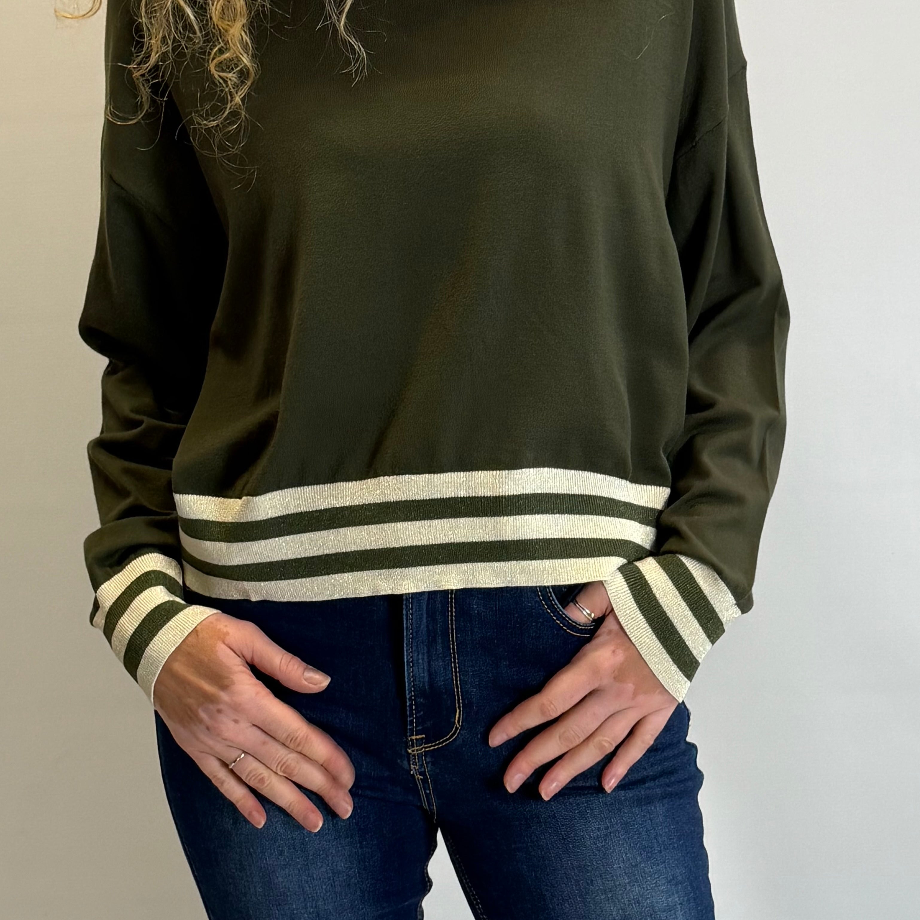 Person wearing an olive green sweater with striped cuffs on a plain background
