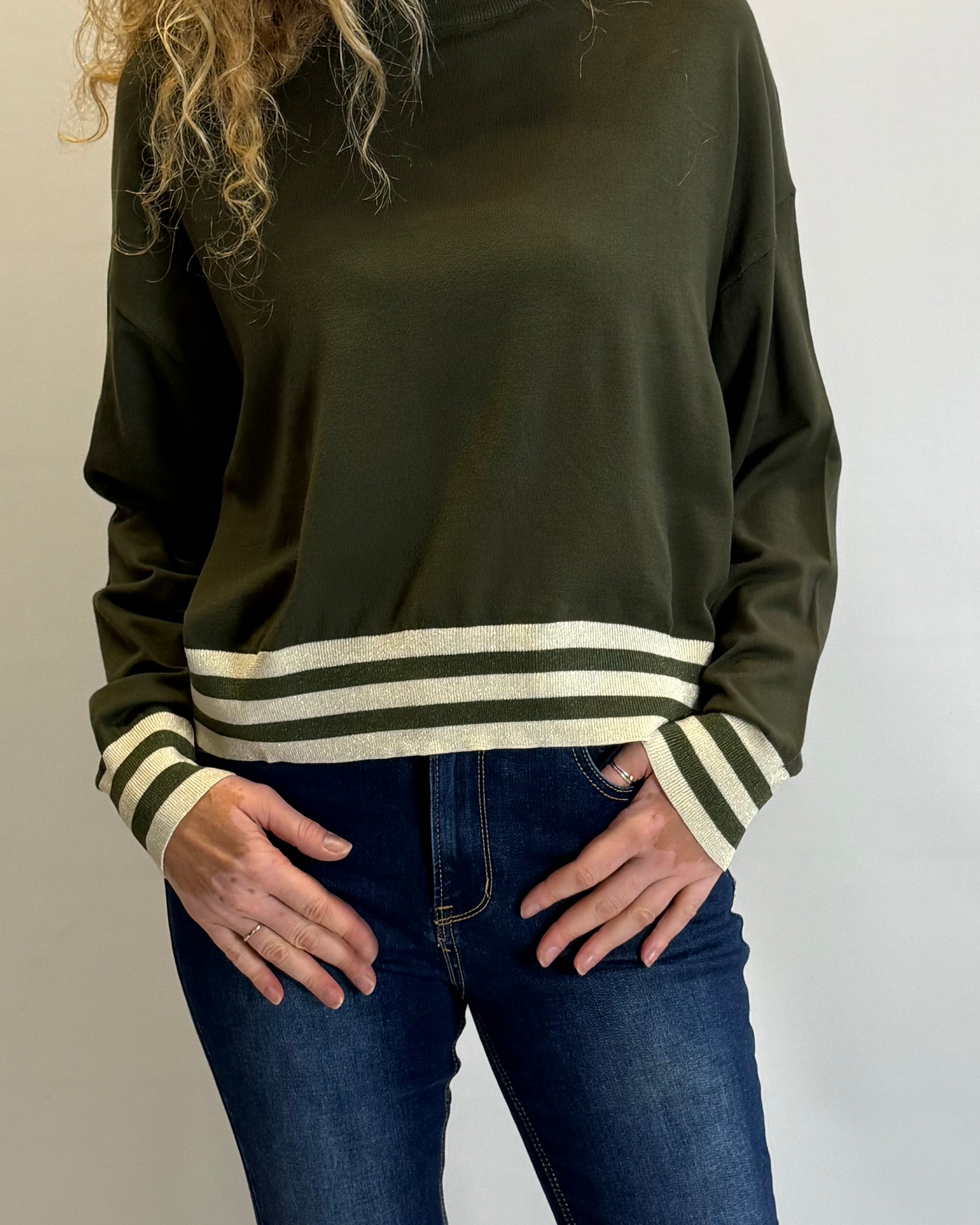 Person wearing an olive green sweater with striped cuffs on a plain background