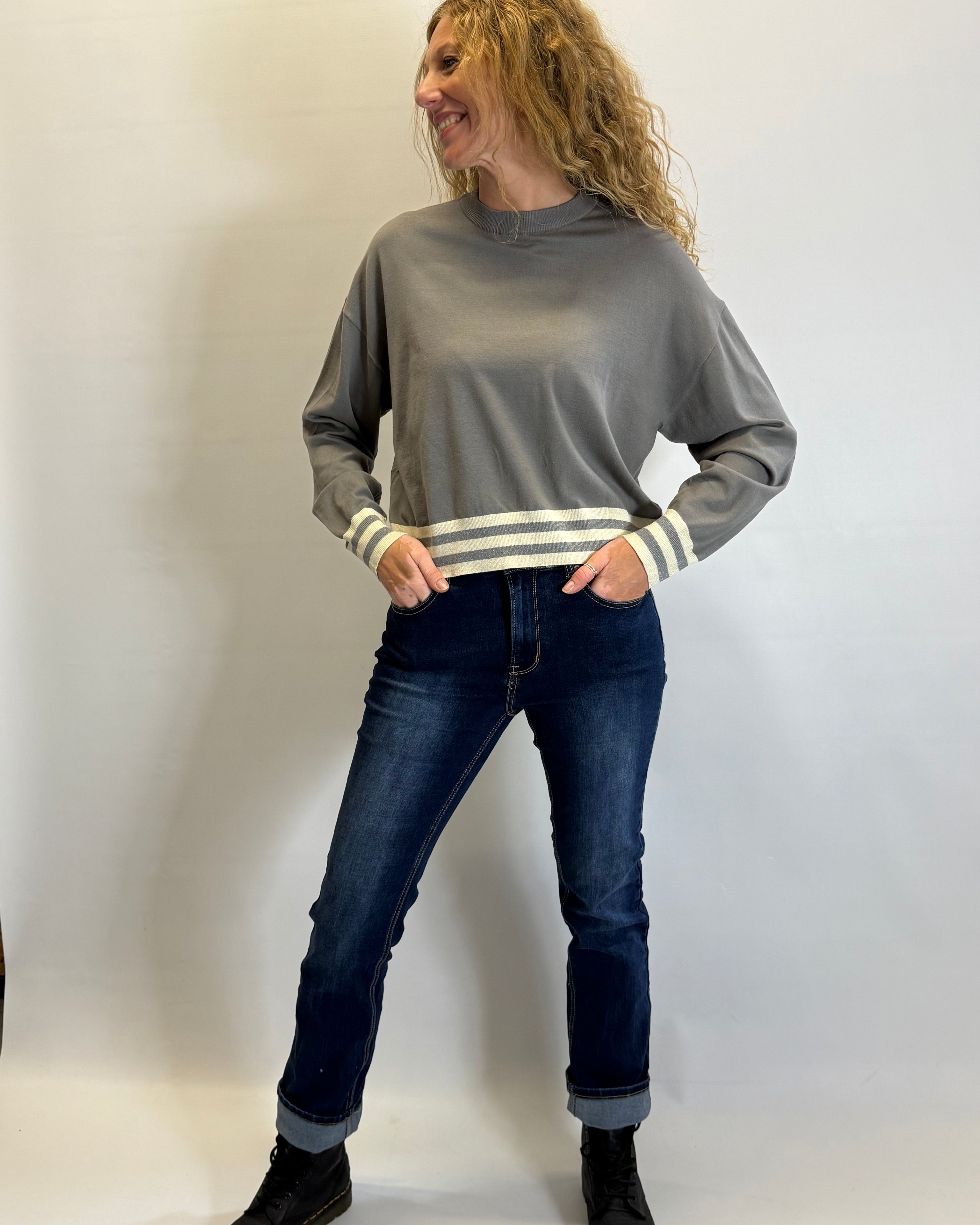 Woman wearing a gray sweater with white stripes and dark jeans against a plain background