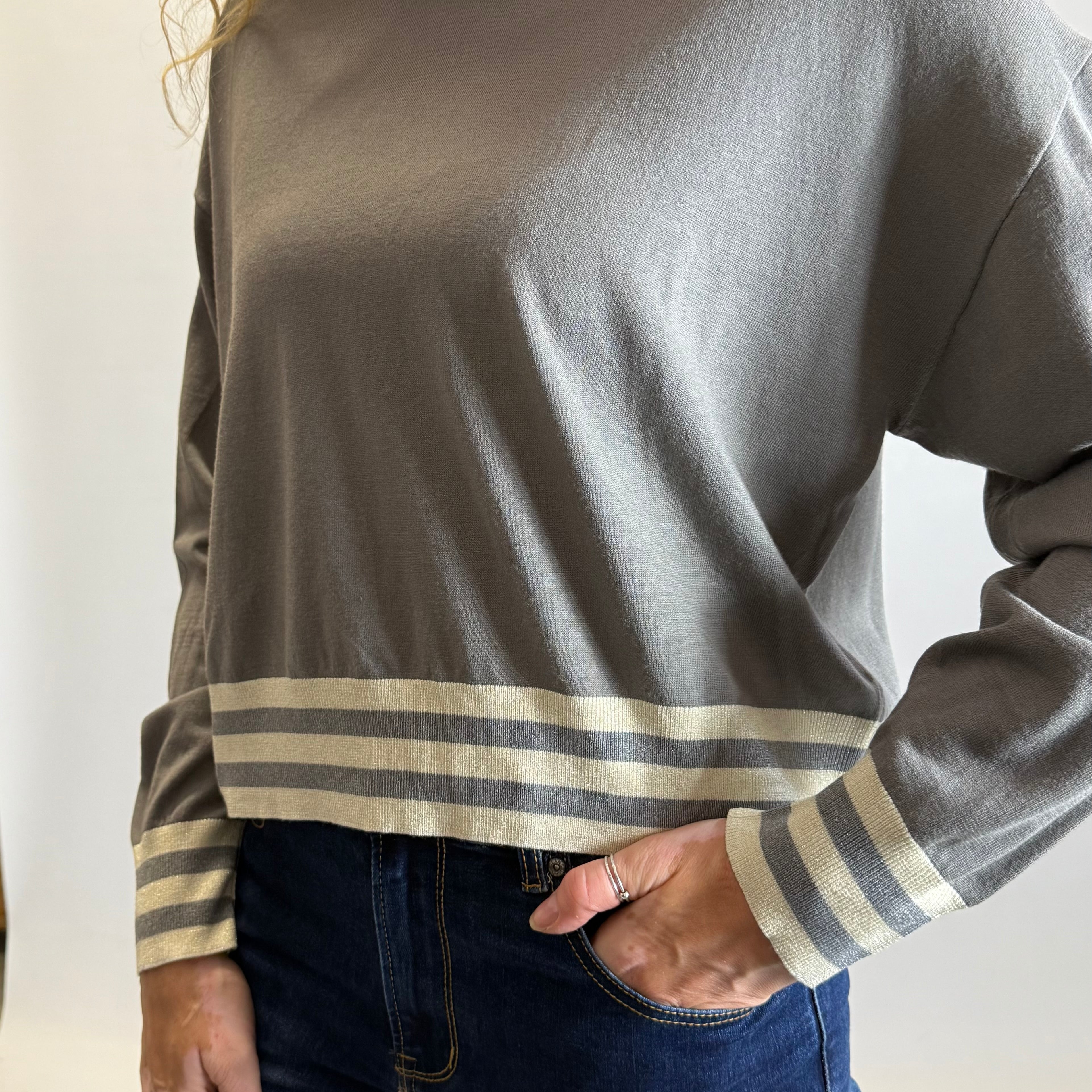 Person wearing a gray long-sleeve shirt with striped cuffs against a neutral background
