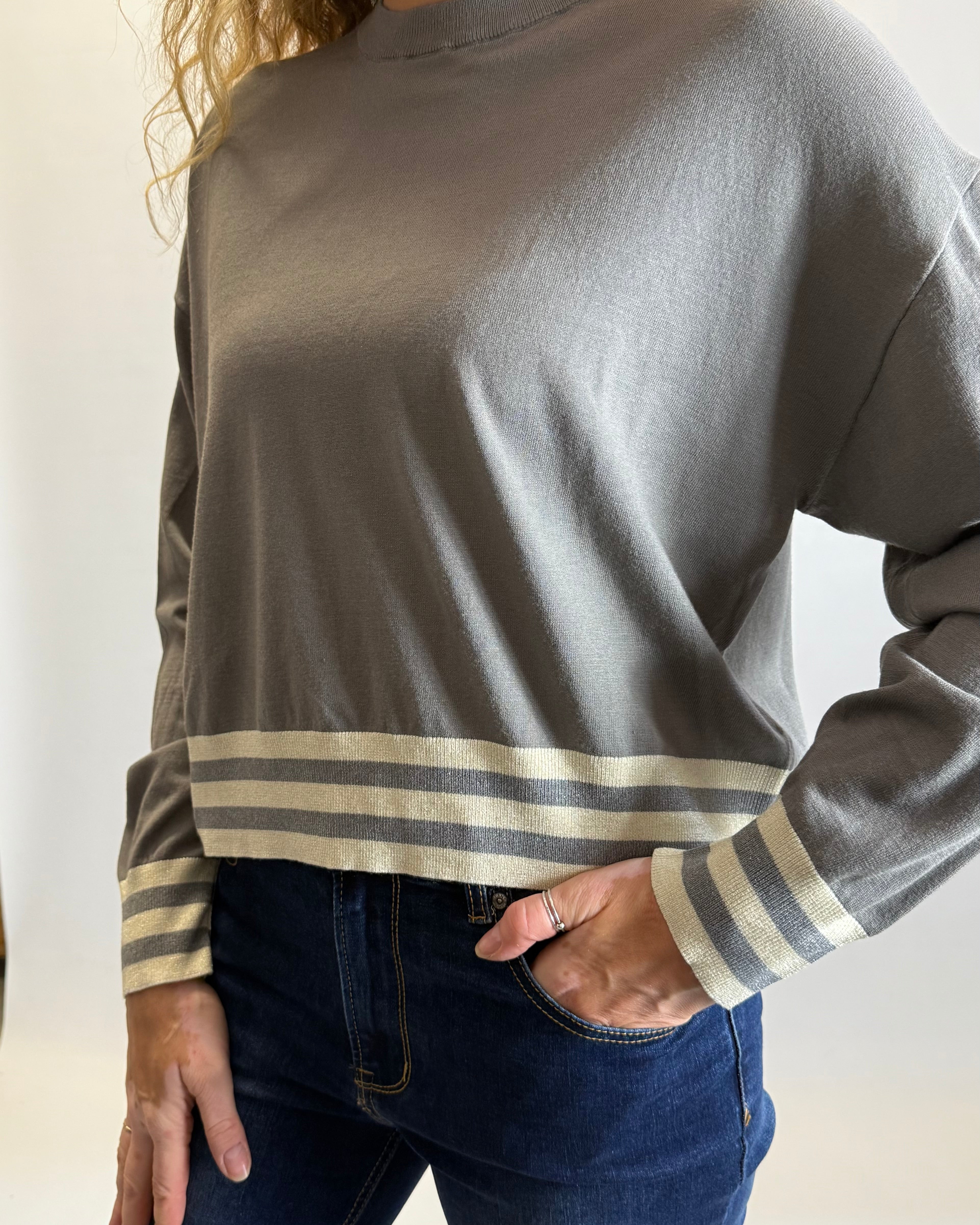 Person wearing a gray long-sleeve shirt with striped cuffs against a neutral background