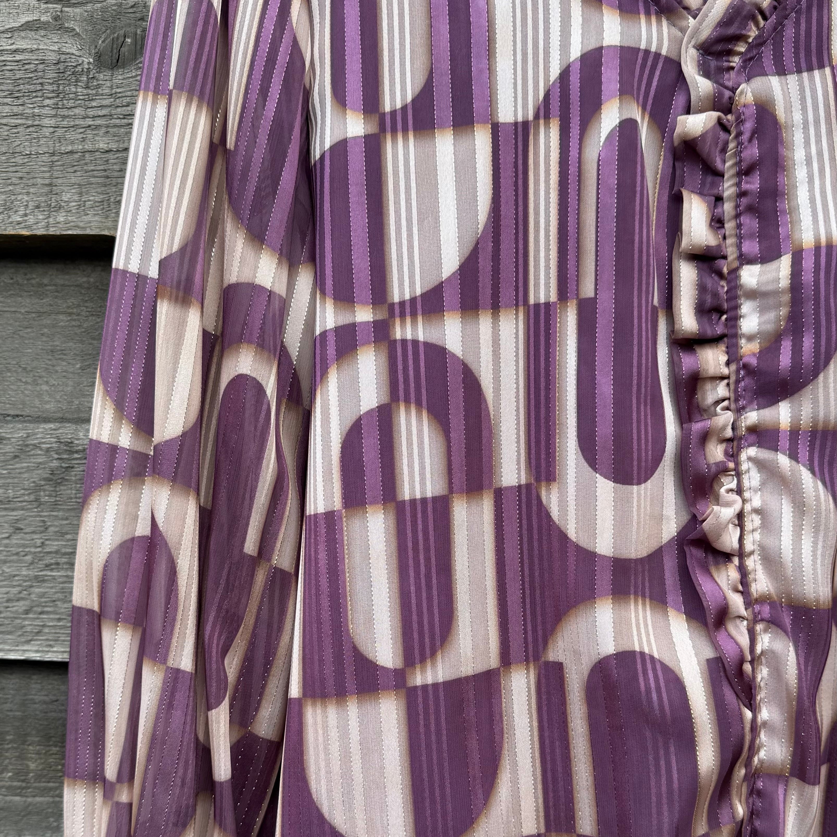 Purple and beige patterned blouse with ruffled details on a wooden surface.