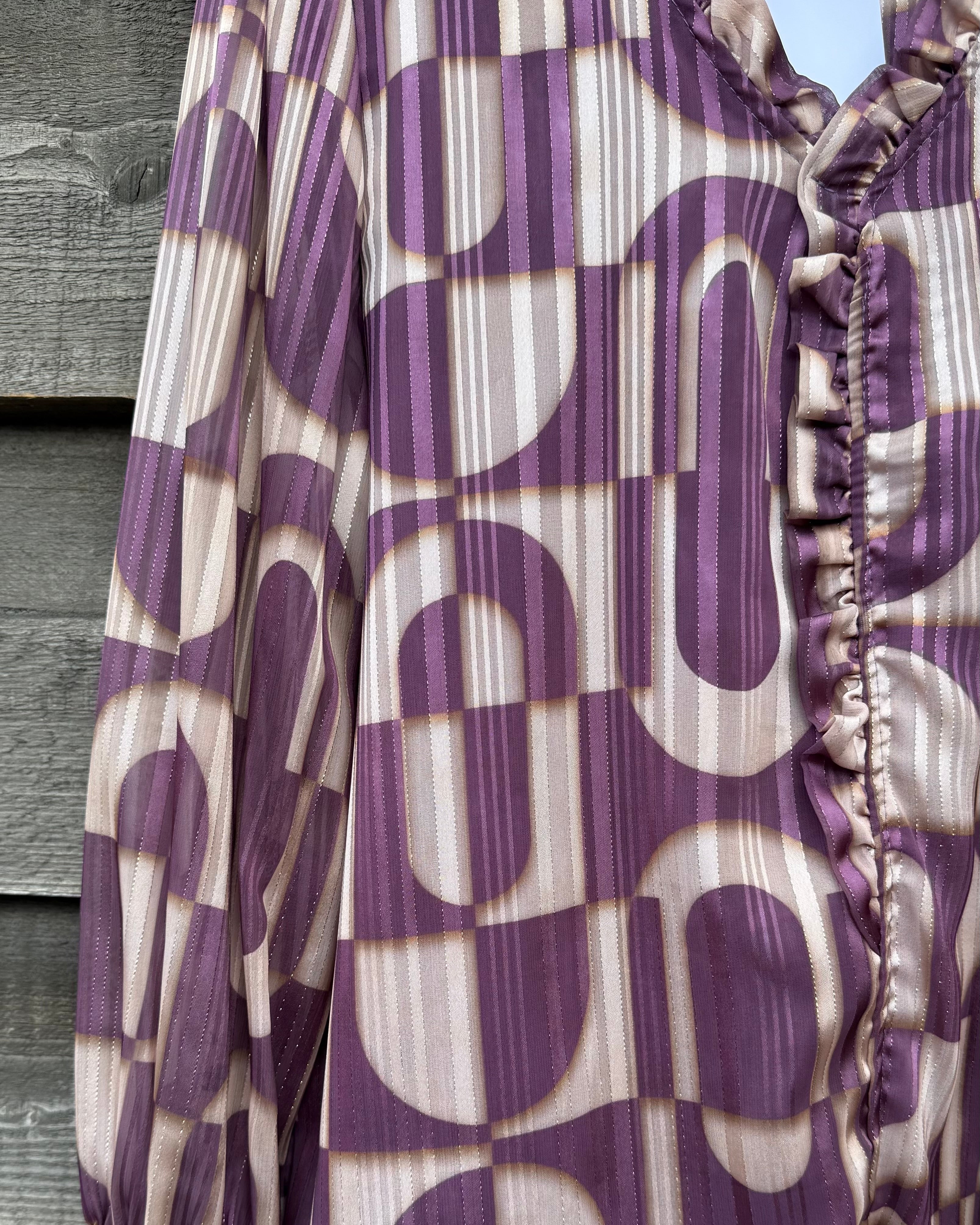 Purple and beige patterned blouse with ruffled details on a wooden surface.