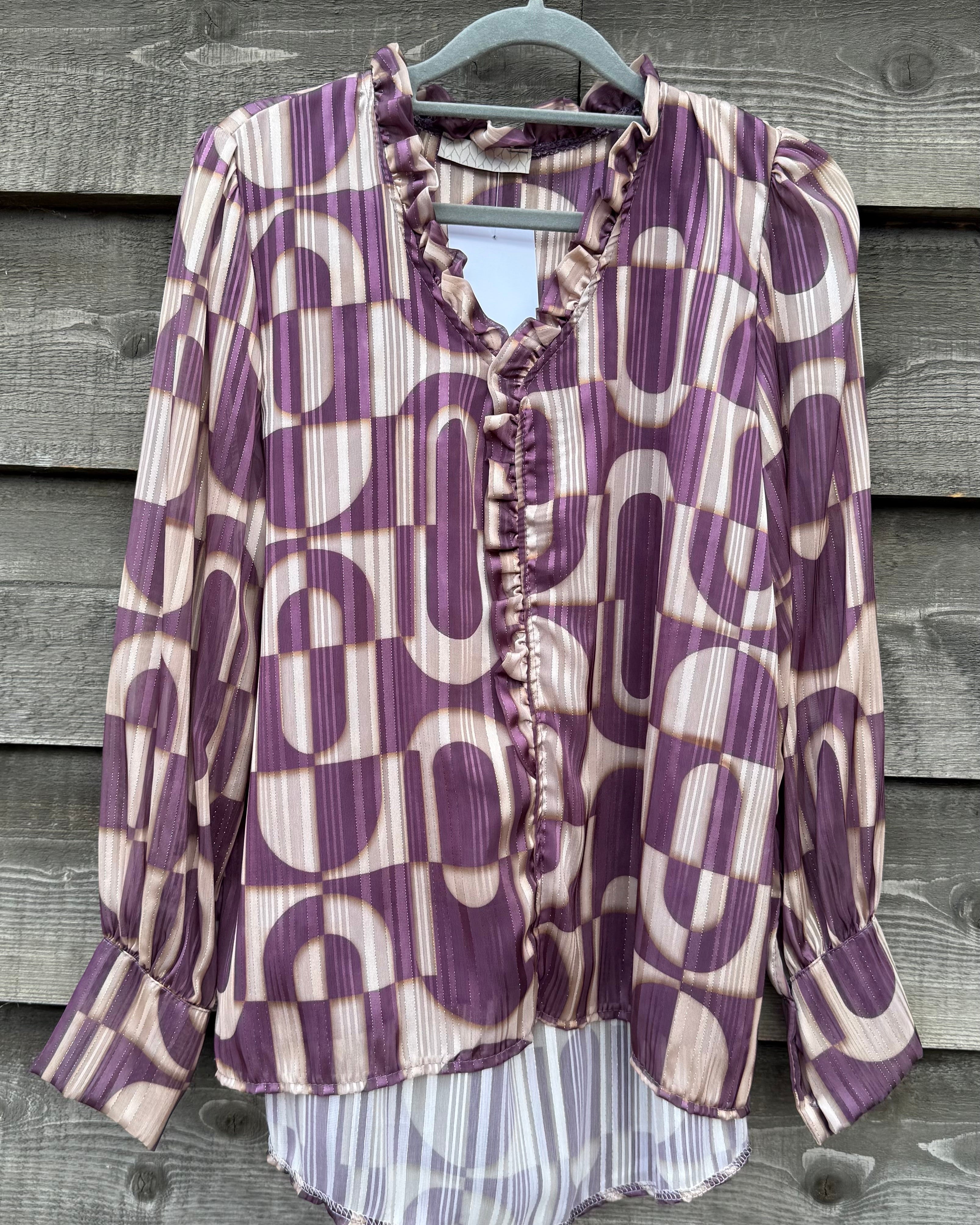 Purple and white patterned blouse on a hanger against a wooden background